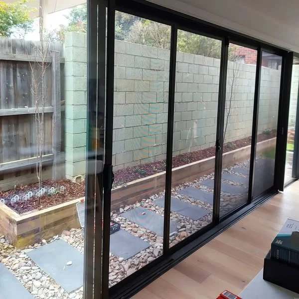 View through glass sliding doors into a small backyard with a stone pathway, gravel, mulch, and a brick wall at the back.
