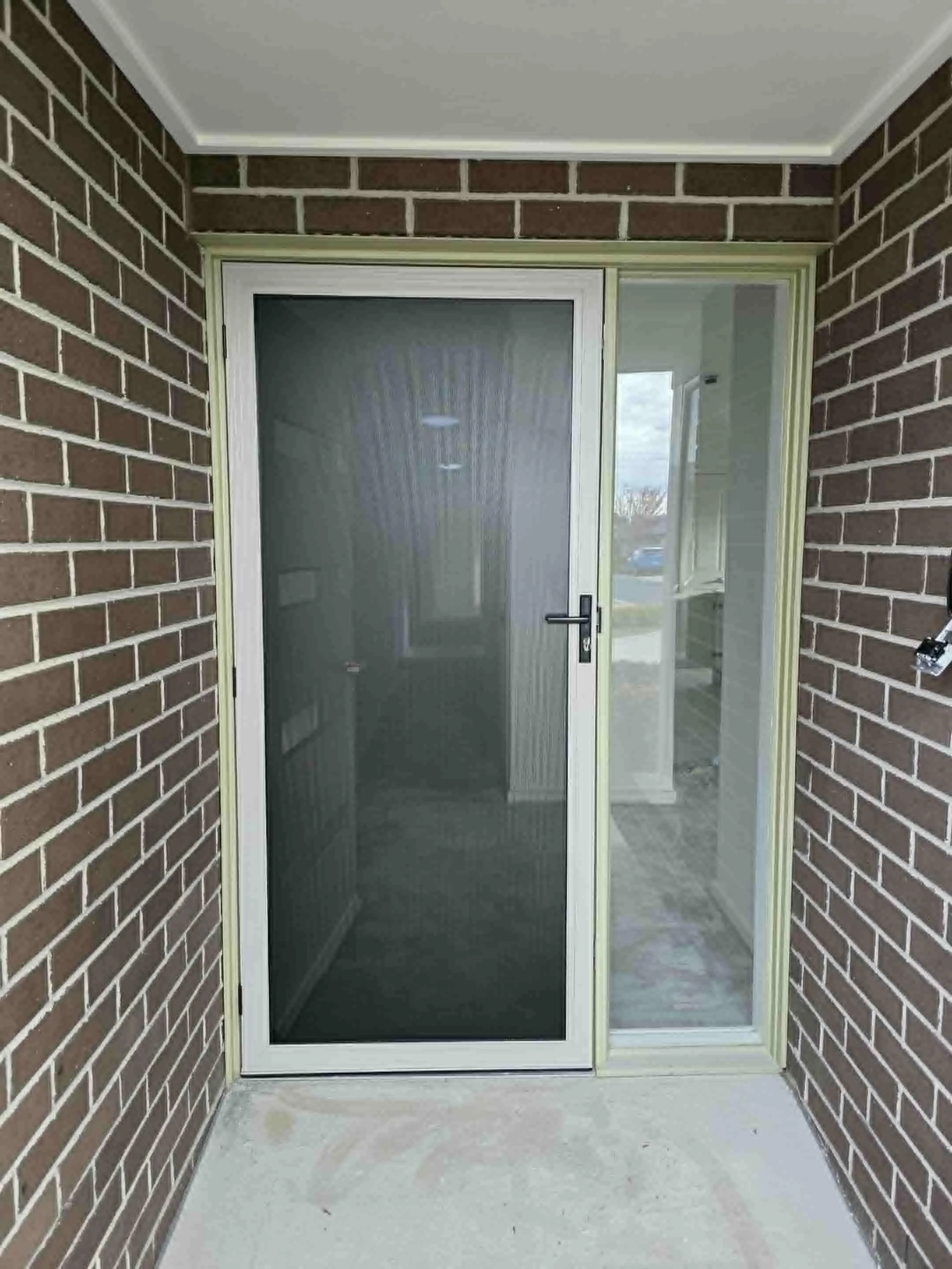 Front door with a screen door and a sliding glass door on a porch with brick walls.