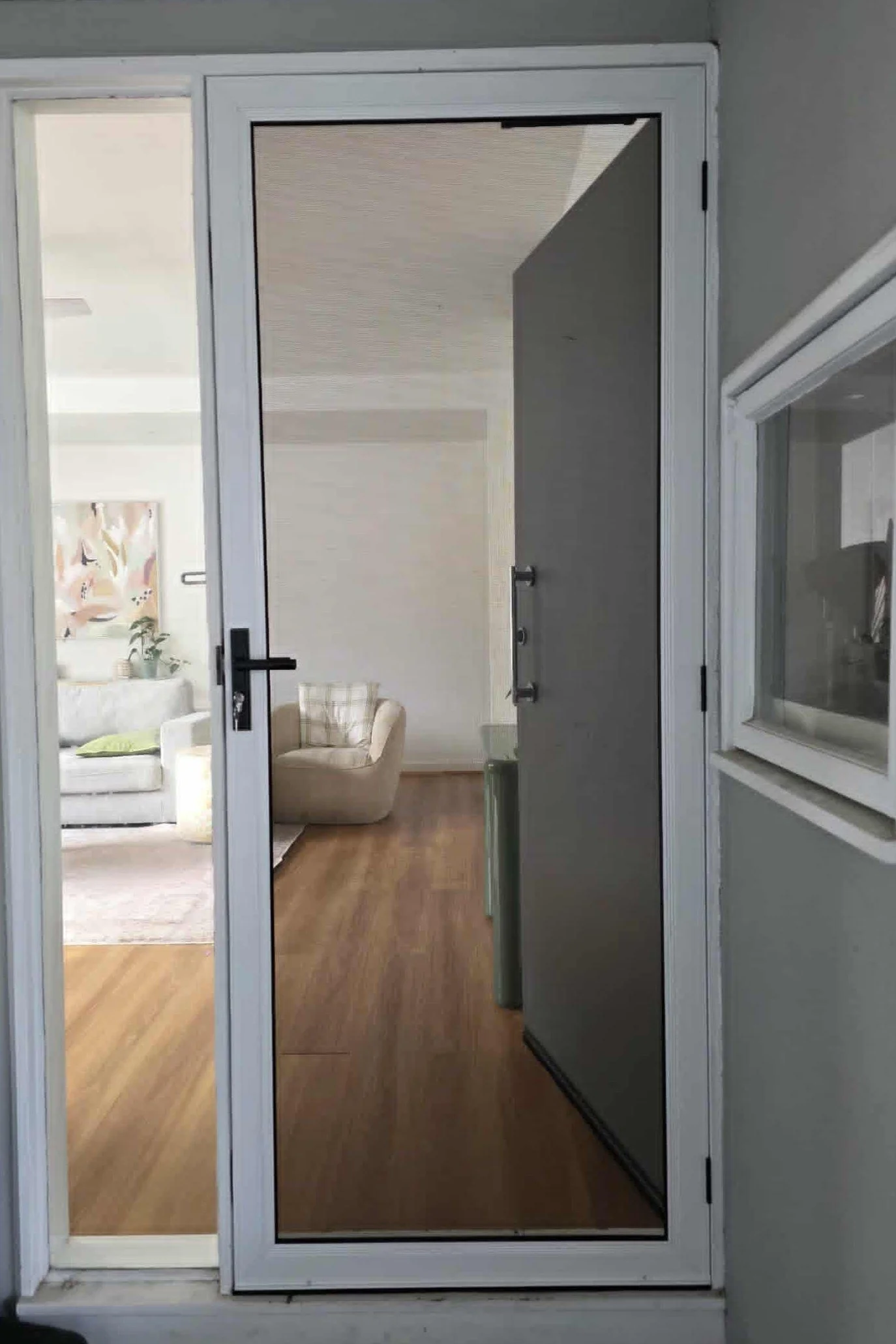A glass door leading into a living room with wooden flooring, beige sofas, and artwork on the wall.
