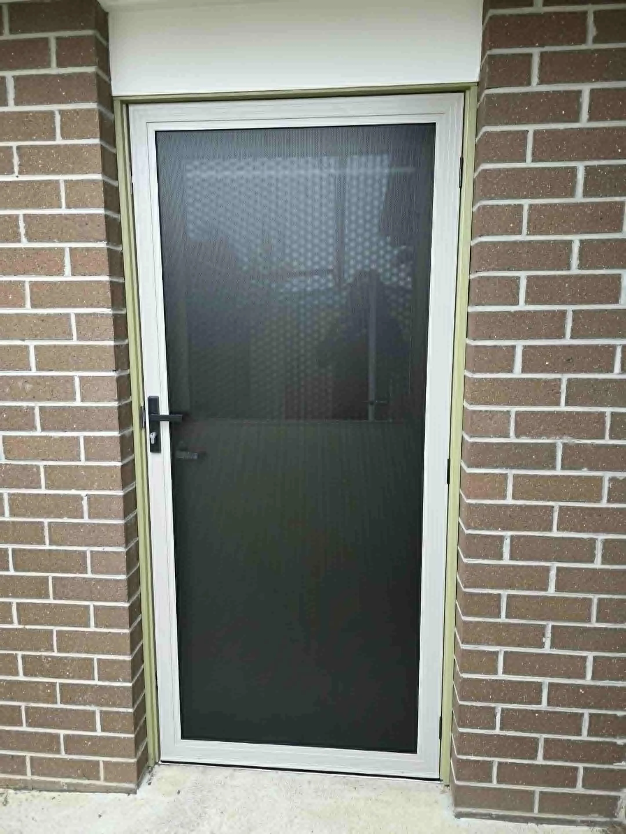 A black screen door with a mesh screen in a brick wall wall.