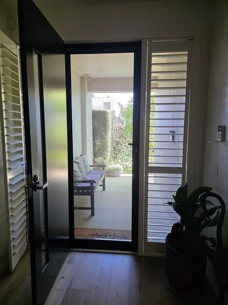 Open front door leading to a porch with seating and greenery outside.