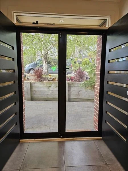 View through glass door to sidewalk with plants and parked car outside.