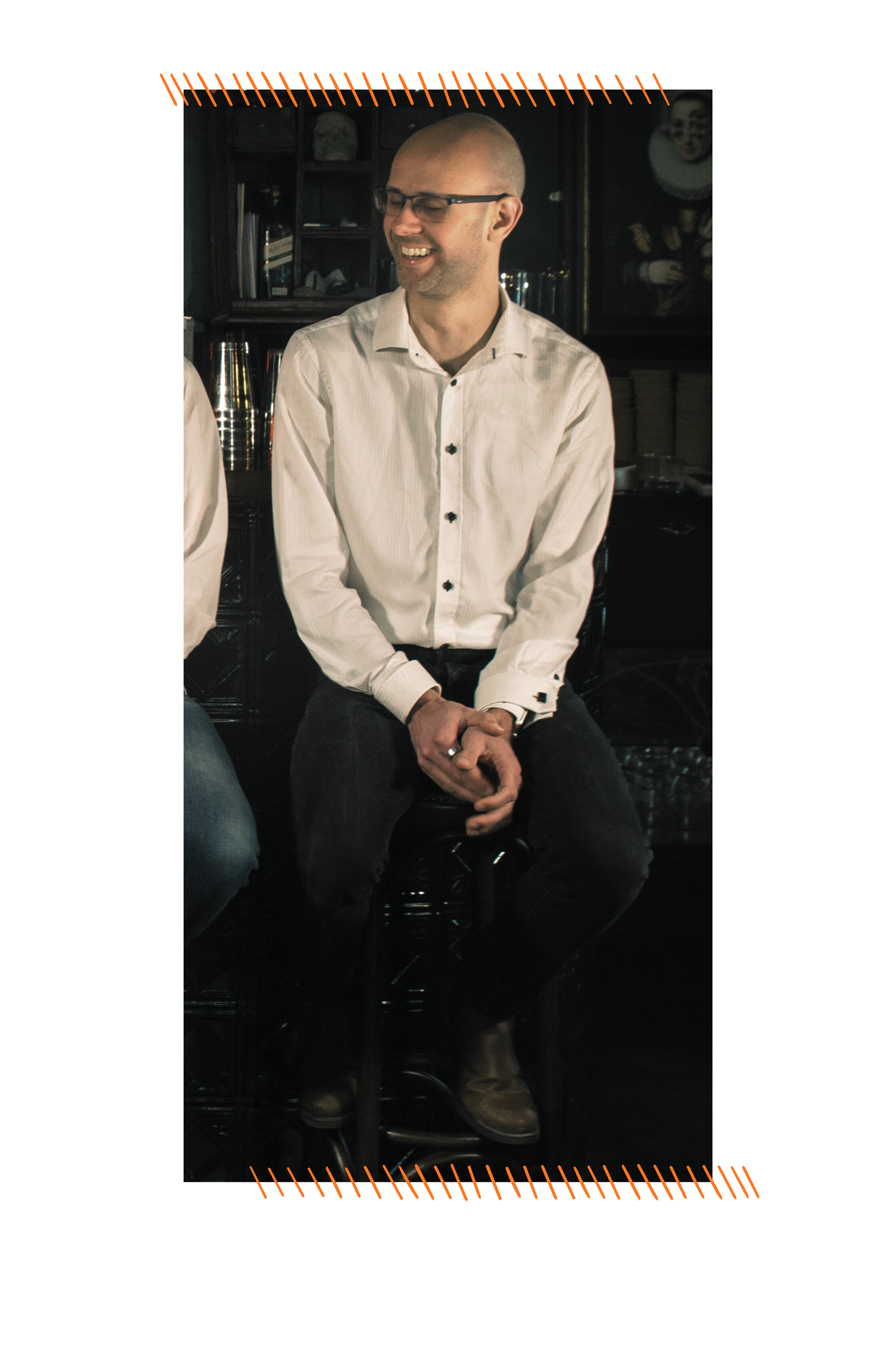 James, a white man with a shaved head and glasses, looks to his band members wearing a white shirt and jeans