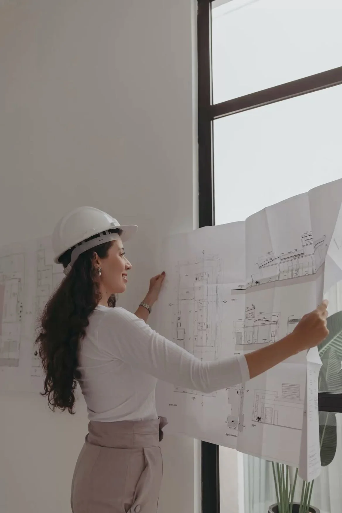 Donna con casco da ingegnere che guarda disegni architettonici su una parete
