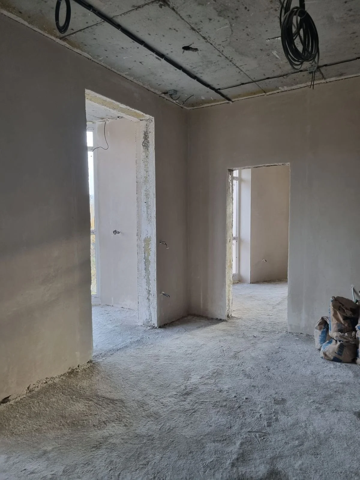 Interno di un appartamento in costruzione con pareti e soffitto in fase di finitura, pavimento grezzo, porte e finestre installate, cablaggi elettrici nelle pareti e sul soffitto