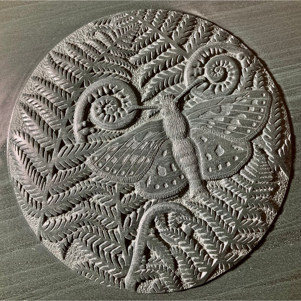 Round metal embossed artwork of a moth with fern leaves and curled fern fronds in the background.