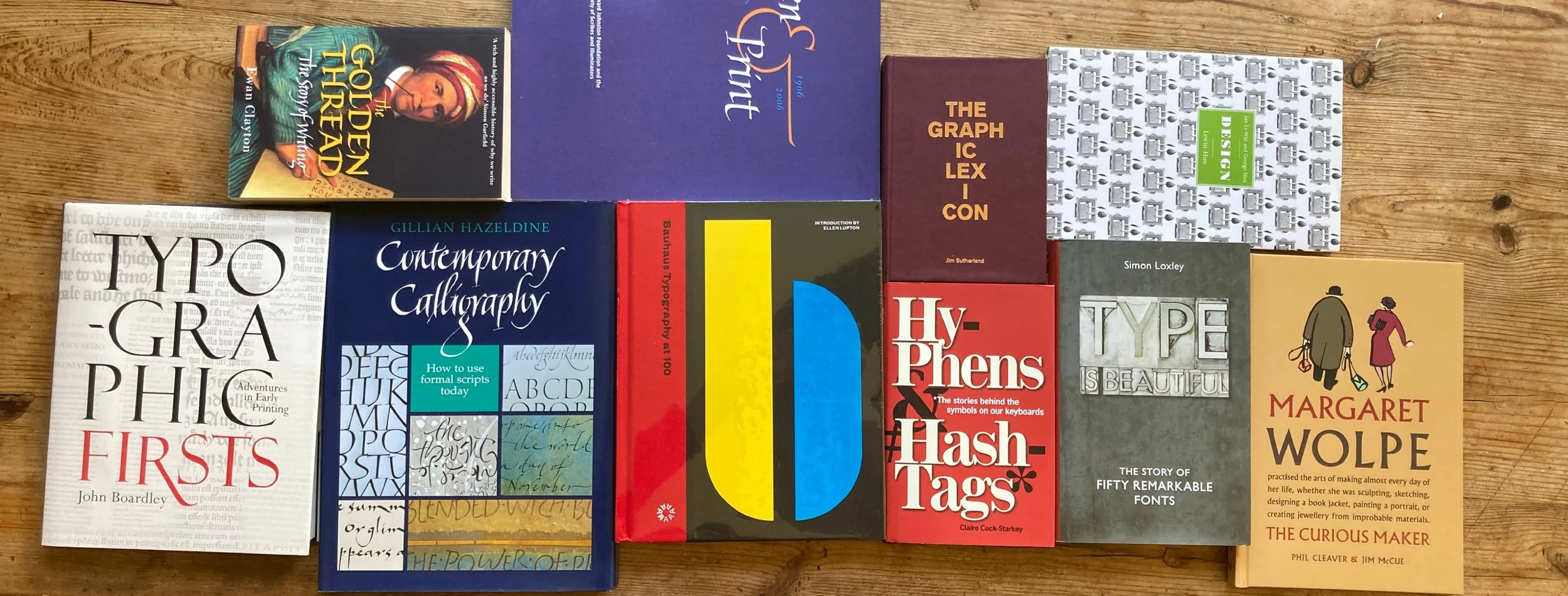 Collection of various books on topics such as typography, calligraphy, design, and history, arranged on a wooden surface.
