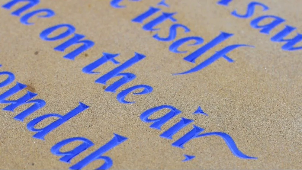 Close-up of blue engraved text on a tan, textured surface, possibly a plaque or sign.