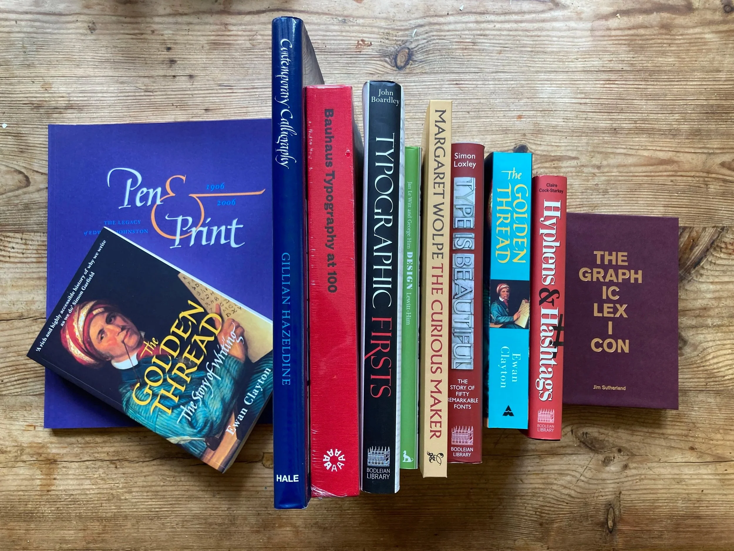A row of books standing upright on a wooden surface, with one book slightly angled and overlapping another. The titles include "Pen & Print," "Gutenberg Revolution," "Bauhaus Typology," and "Typosopher."