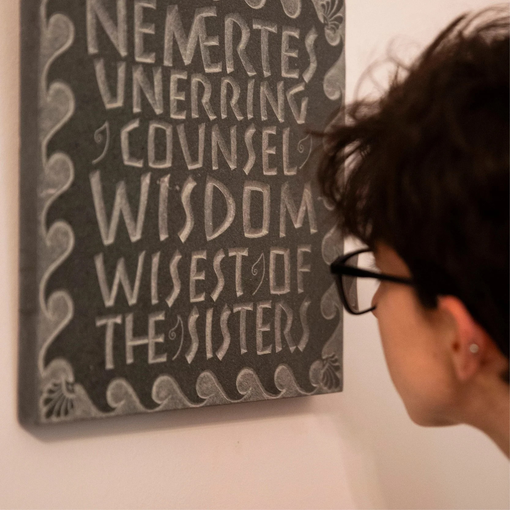 Close-up of a person with dark hair and glasses looking at a chalkboard with handwritten decorative lettering that says 'Thanks for listening. Love, WISDOM.'