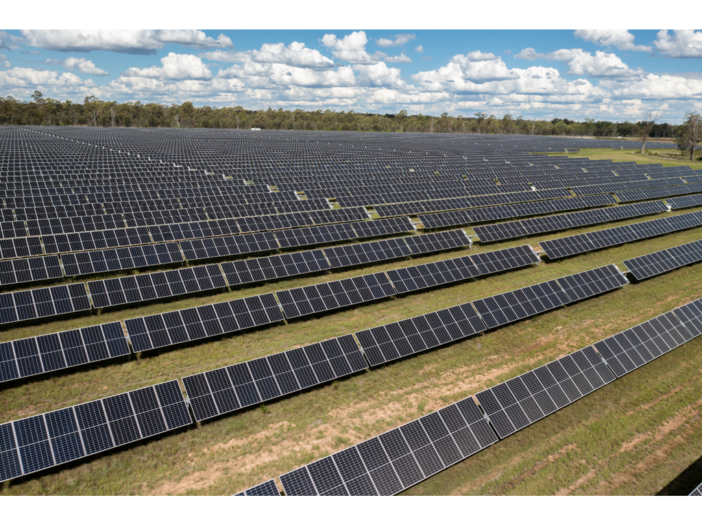 A large field of solar panels under a partly cloudy sky.