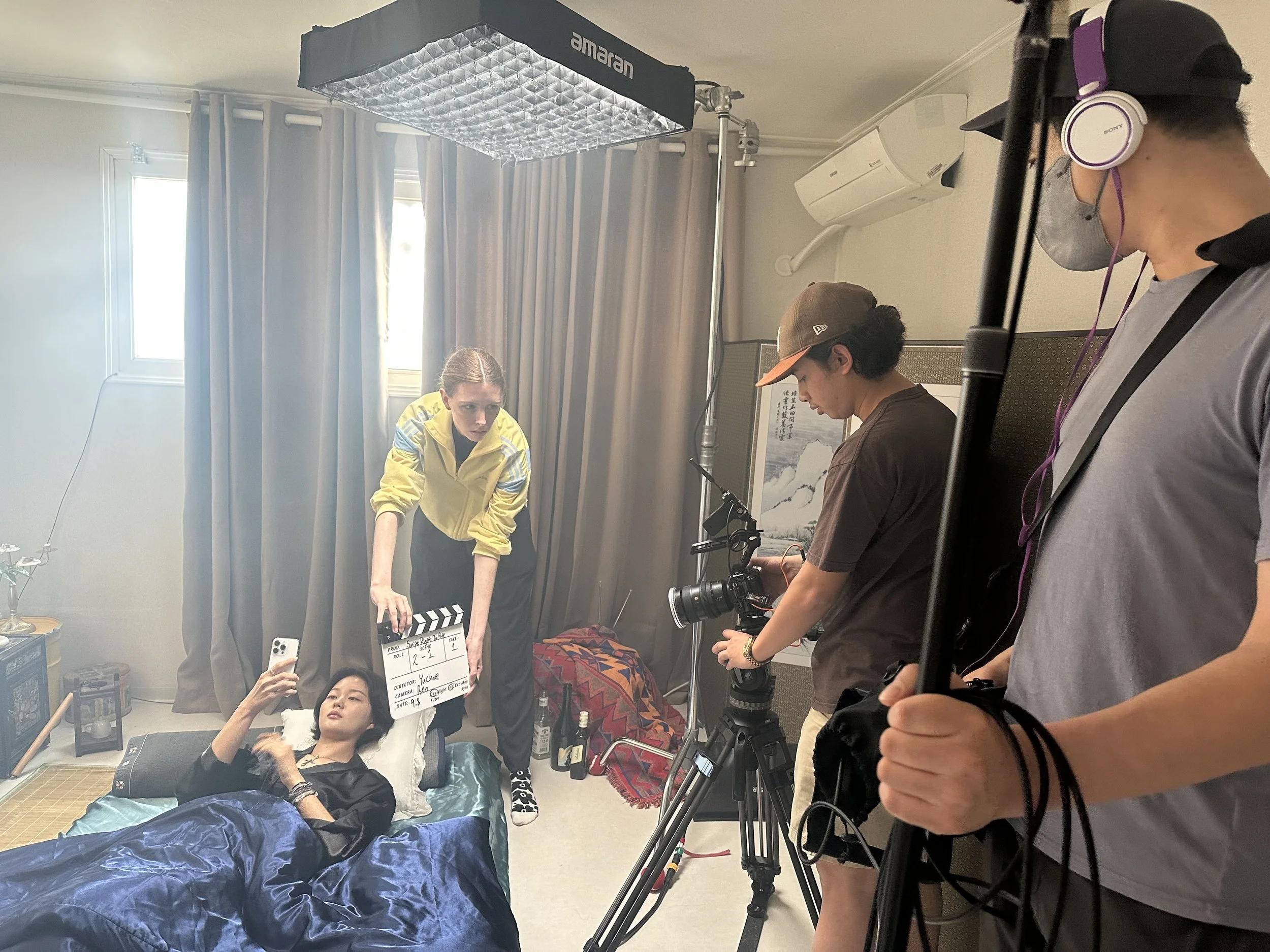 Swipe Right To Bite/SRTB behind the scenes/BTS. Jiseo (Yeon) in bed with production crew hitting slate for next take.