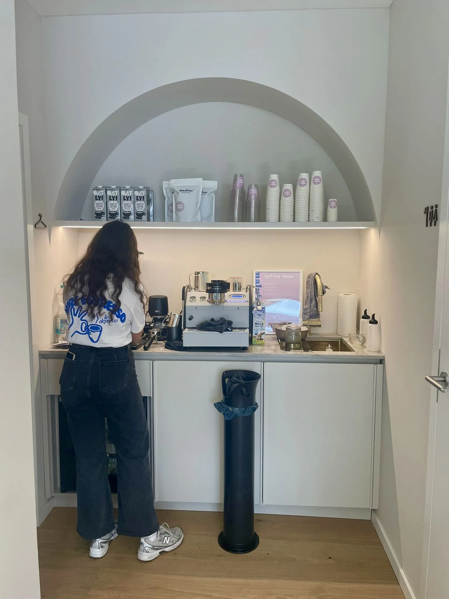 Eine Frau arbeitet hinter einer kleinen Café-Bar mit Espressomaschine, Tassen und Roestbar Bio Kaffee Packungen auf dem Regal über der Theke.