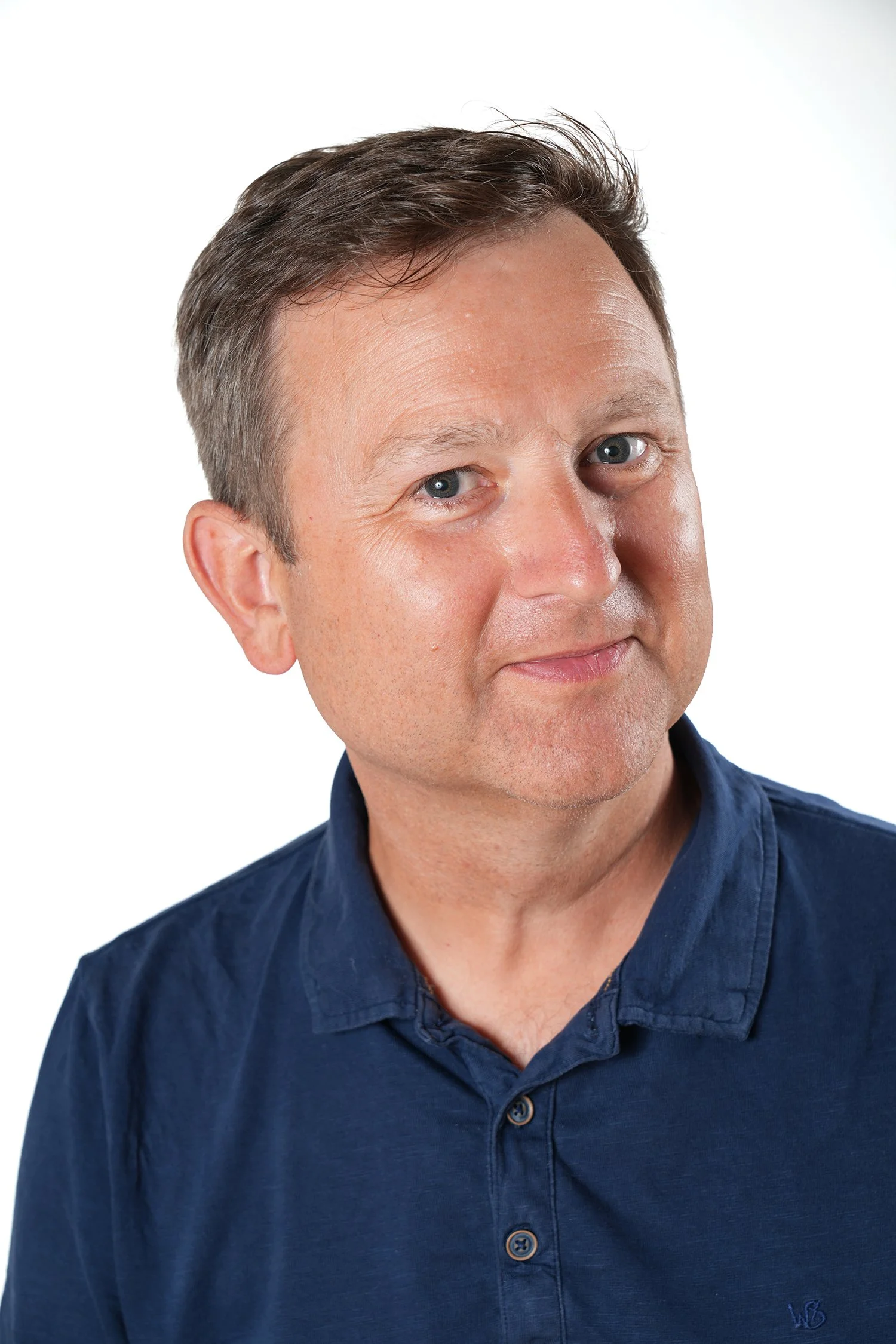 Photo of Alex showing head and shoulders, smiling to the camera wearing a dark blue polo shirt against a white background