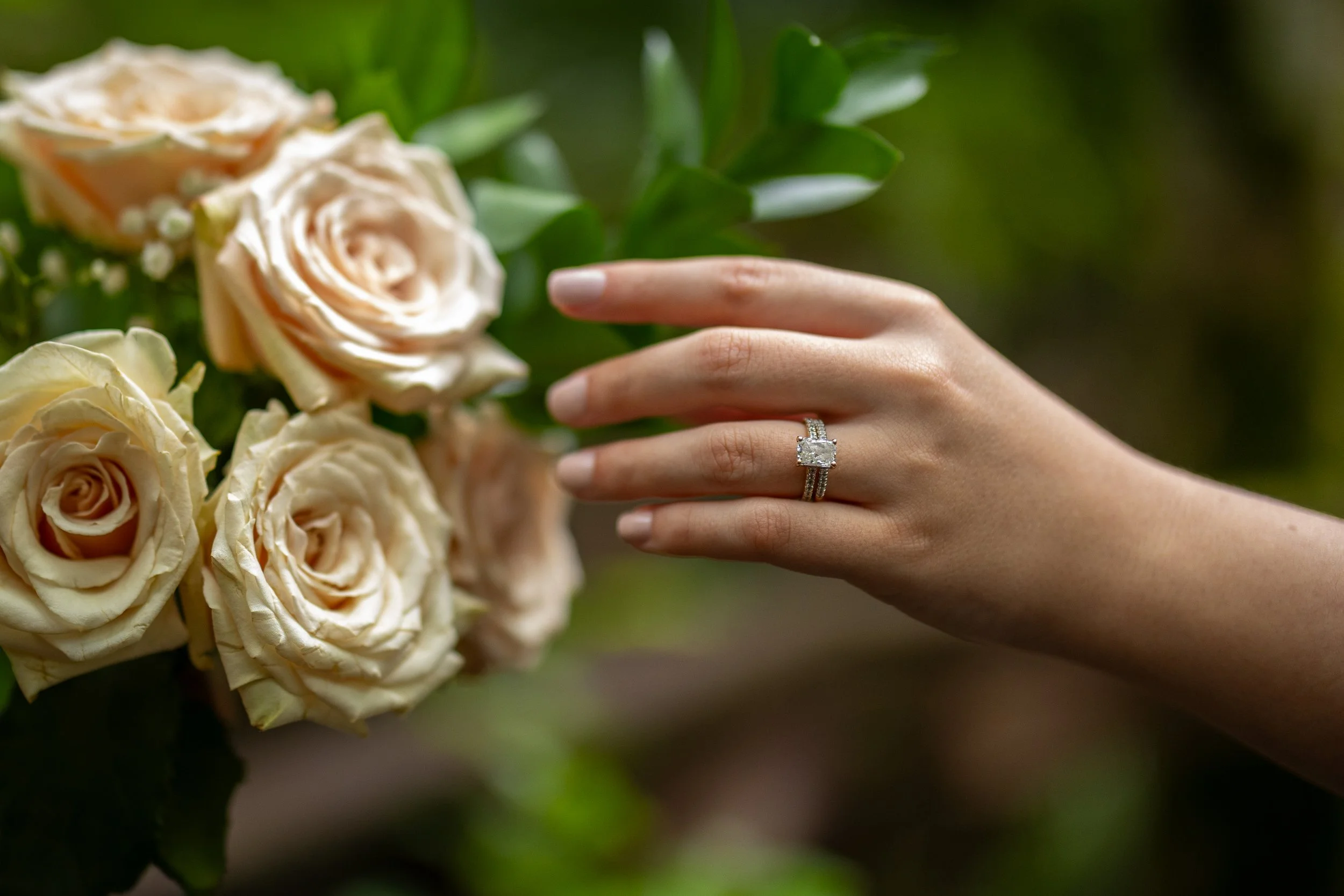 A close-up of a person's hand showing an engagement ring, resting on another person's shoulder in an outdoor setting.