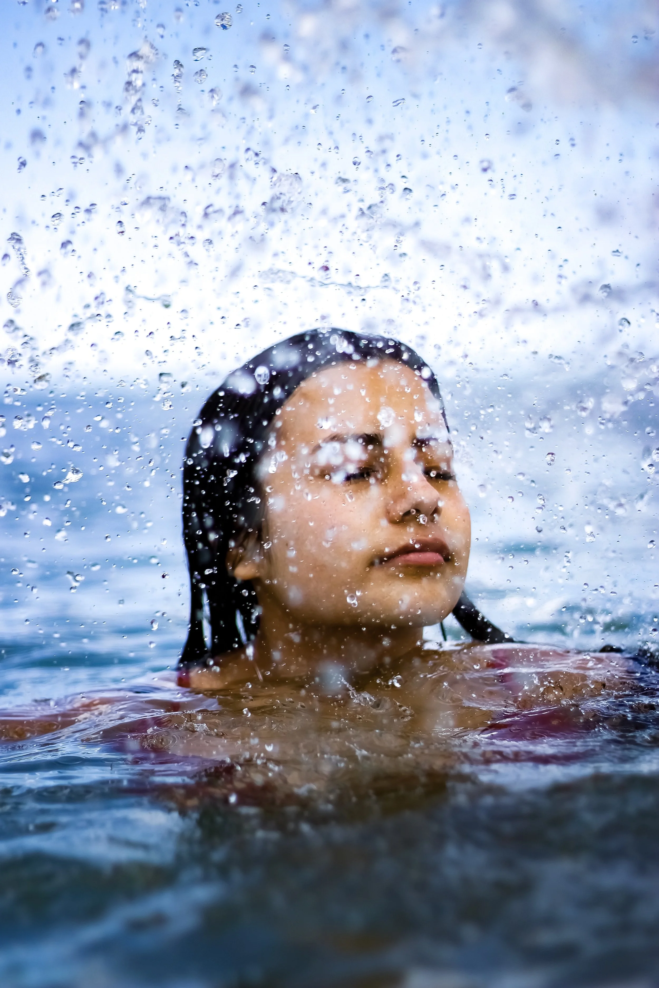 A woman with wet hair and closed eyes floating in water with water splashing around her.