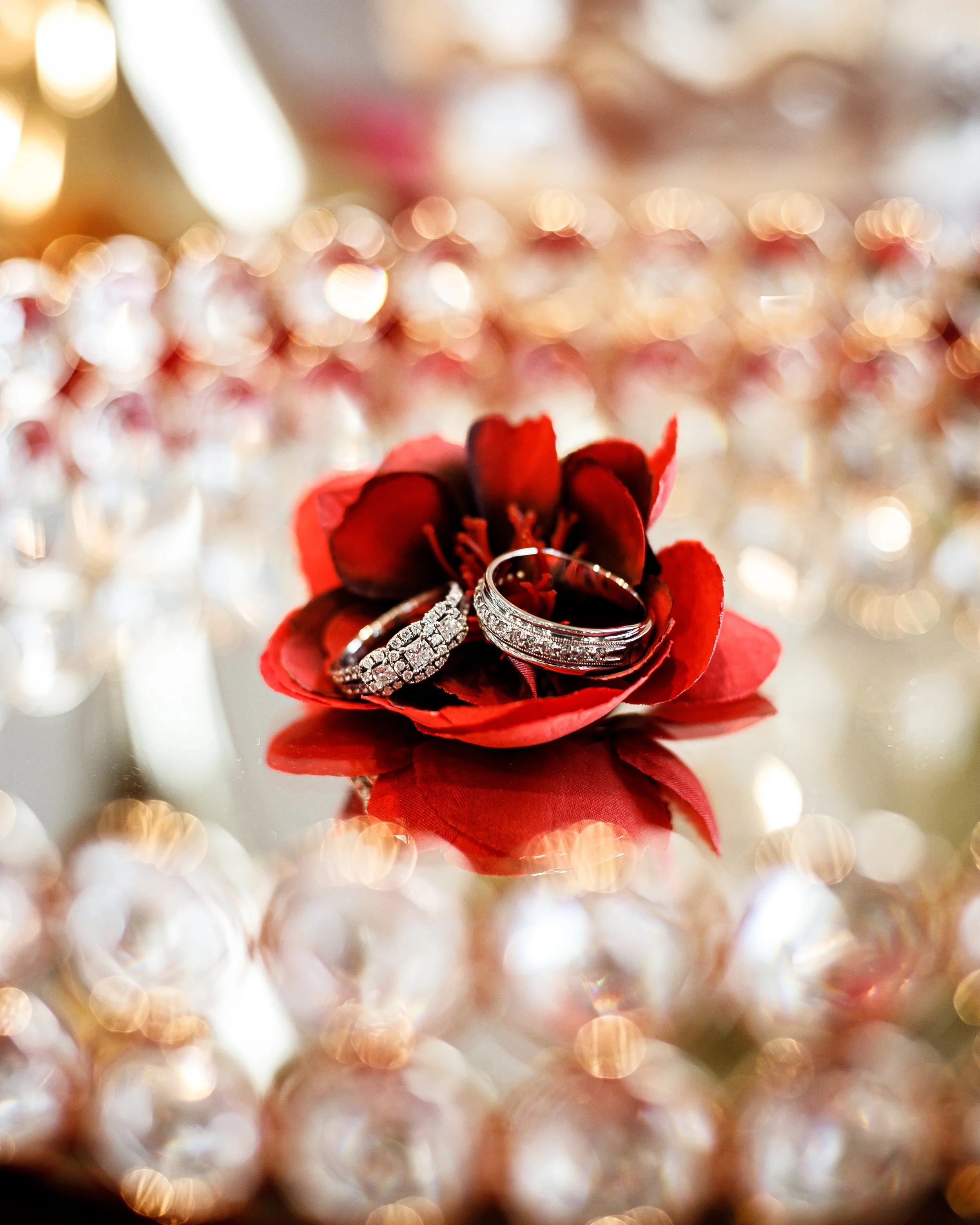 Two diamond rings on a red flower with a blurred gold background.