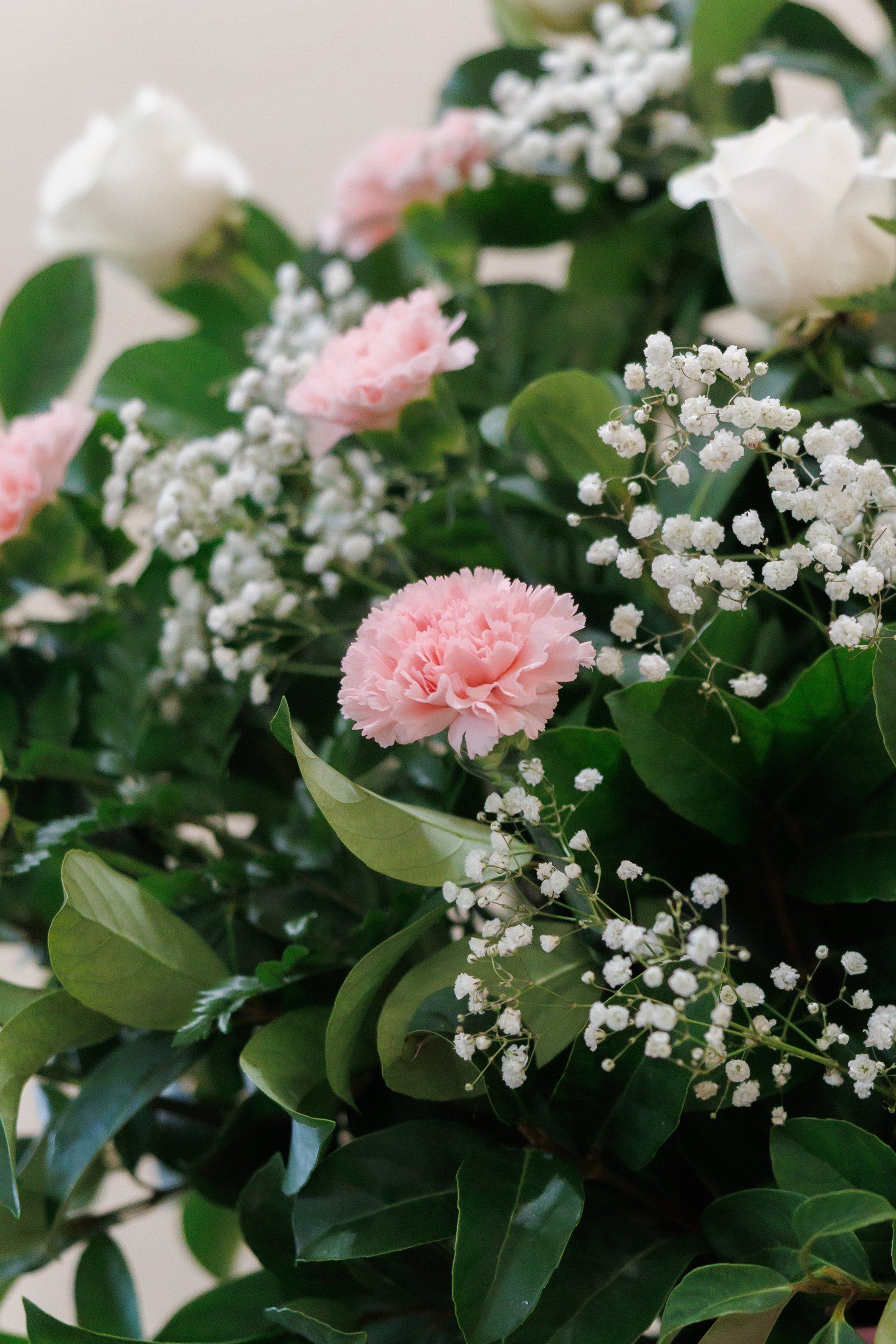 Close-up of a bouquet with pink carnations, white roses, baby's breath, and green foliage.