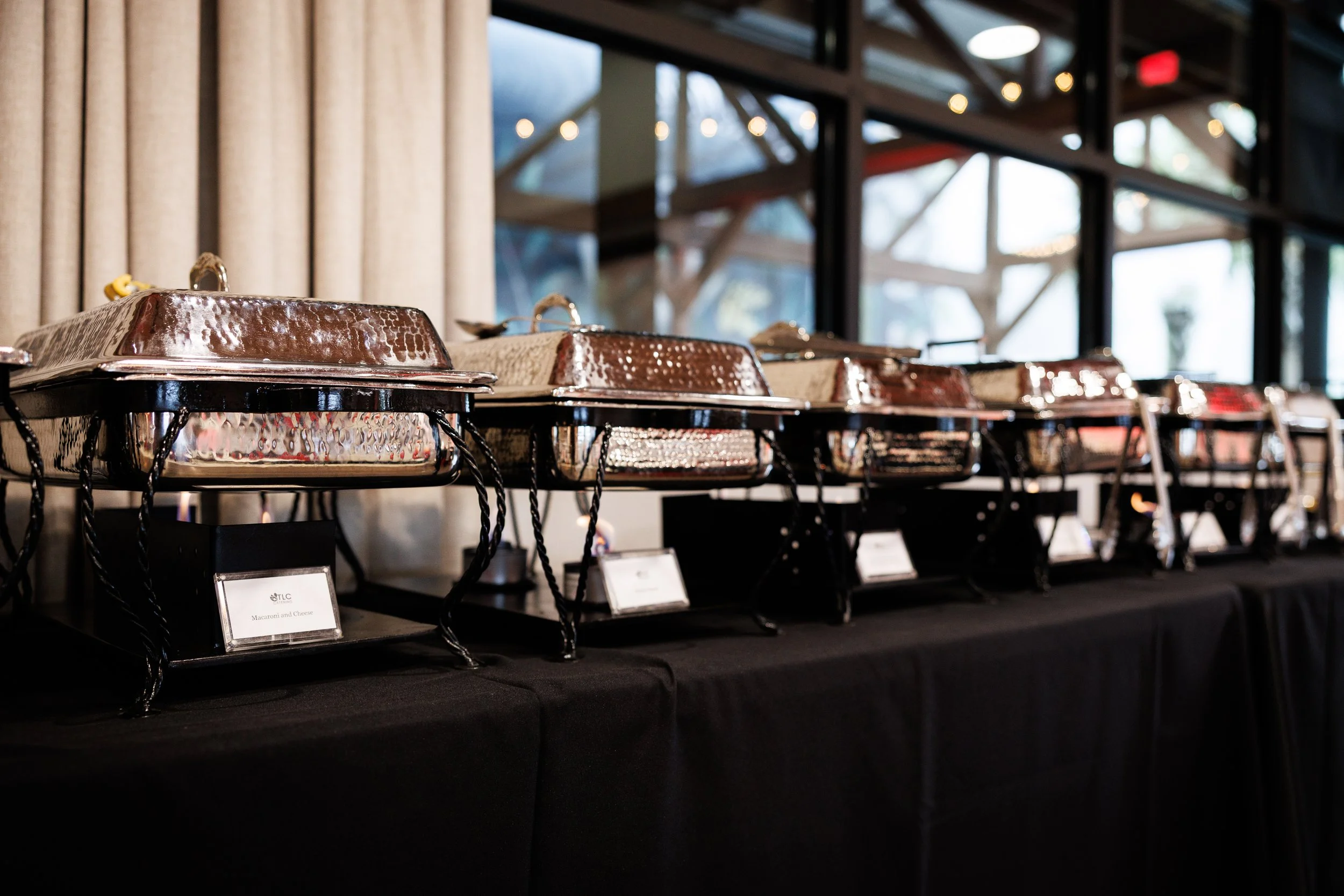 A row of chafing dishes on a black table at a buffet in a modern, well-lit restaurant