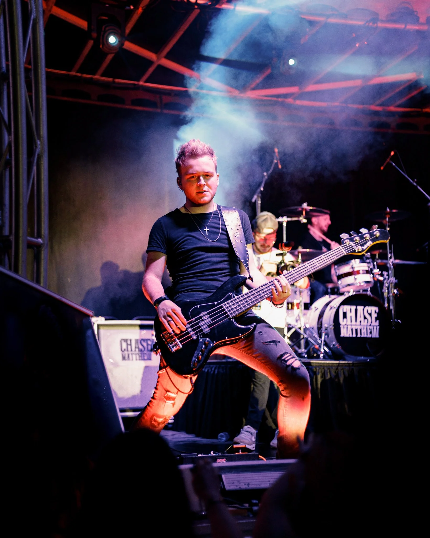 A musician playing a guitar on stage with band members in the background and stage lighting.