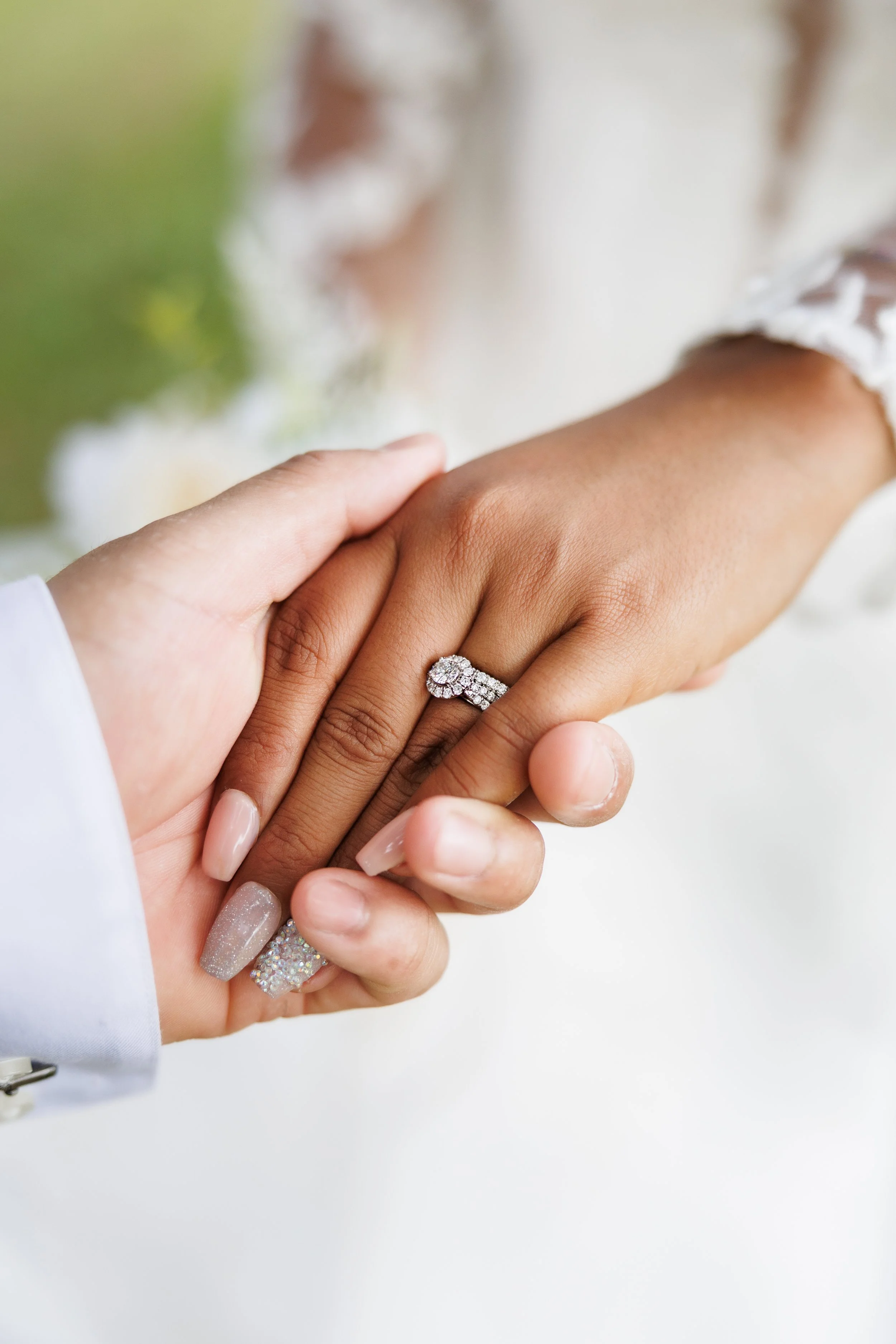 Close-up of two hands holding, one hand with a diamond engagement ring, symbolizing a wedding or engagement.