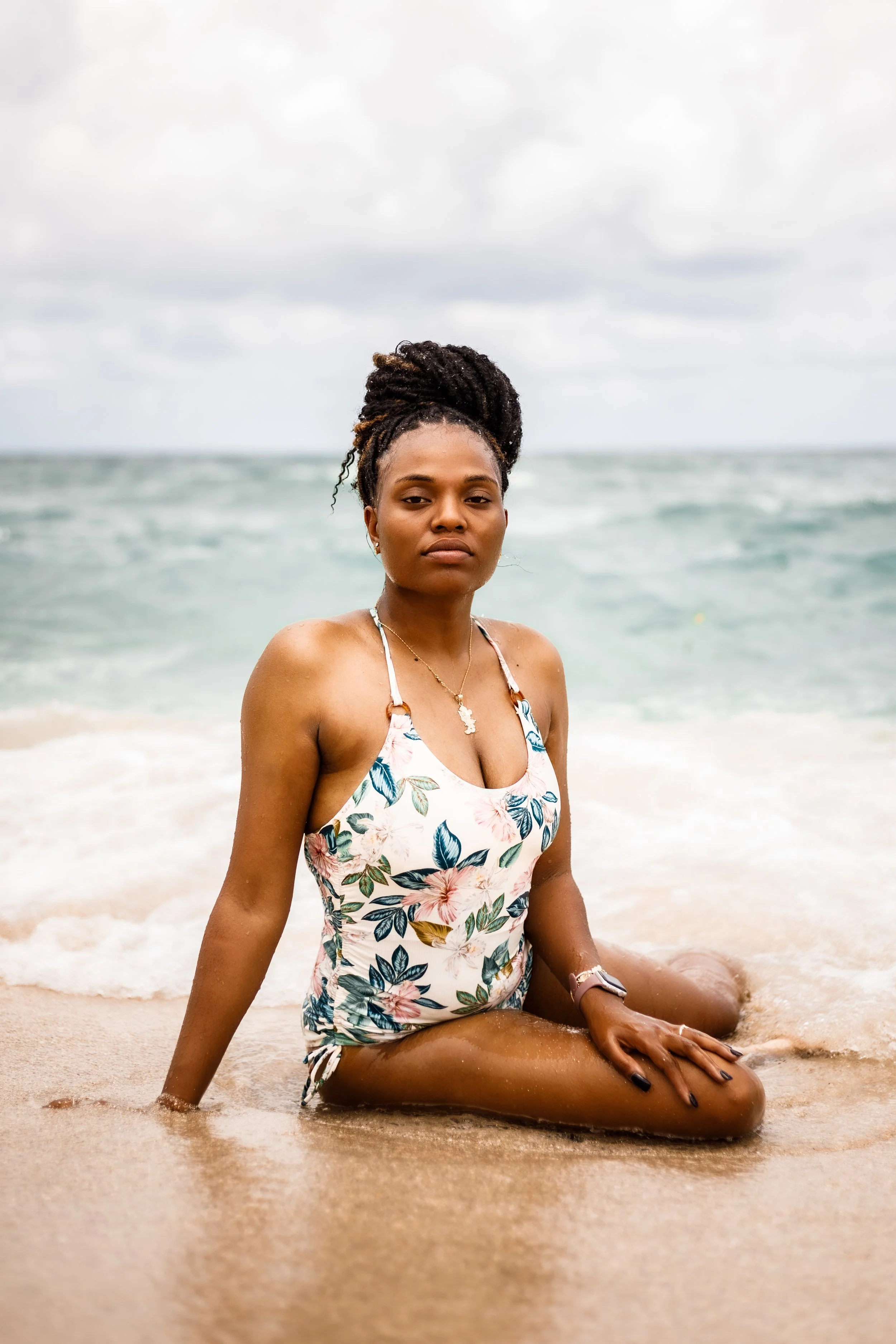 A woman sitting on the beach with ocean waves in the background.