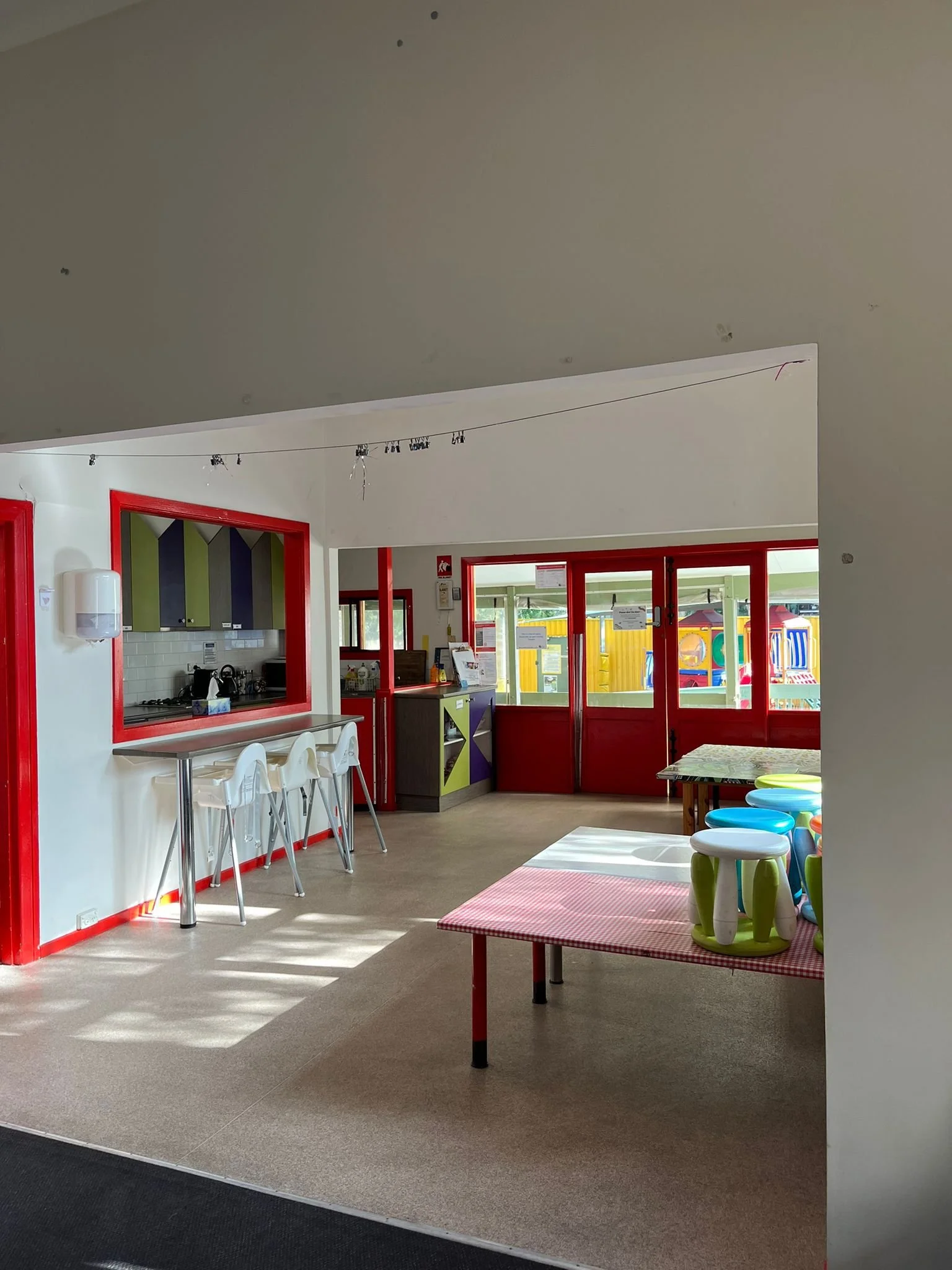 Interior of a children's play or activity area with colorful furniture, tables, and a view of outdoor playground equipment through windows