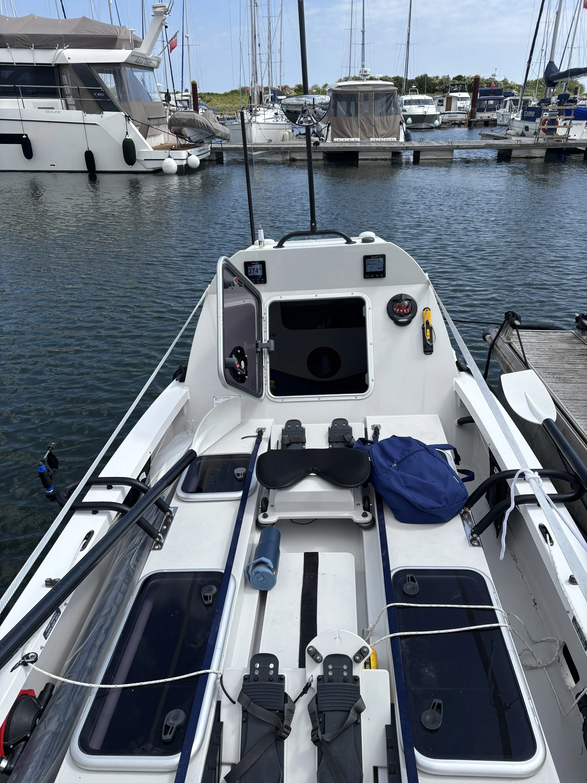 View from the front of a small white fishing or recreational boat docked at a marina, with boats and yachts in the background.