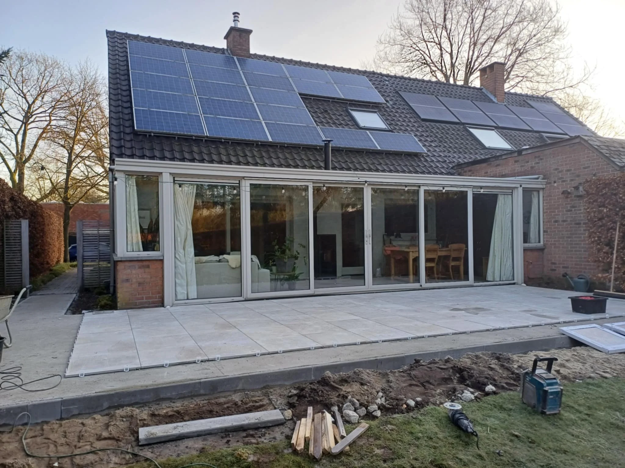 Tuin met nieuwe betegelde terras en zonnepanelen op het dak.