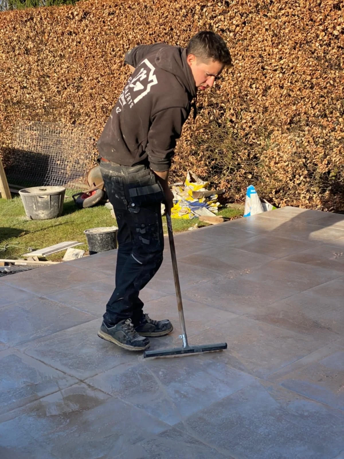 Michiel Schouwaerts aan het betegelen van een terras met grote steentegels.