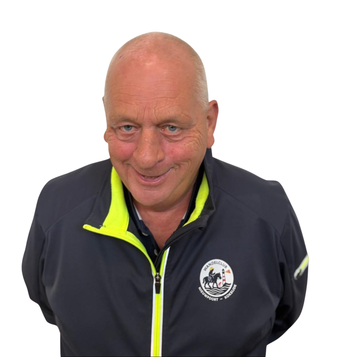 Een oudere man met een glimlach, wit haar en blauwe ogen, gekleed in een donker sportjack met een geelrits en een logo van een wandelclub.