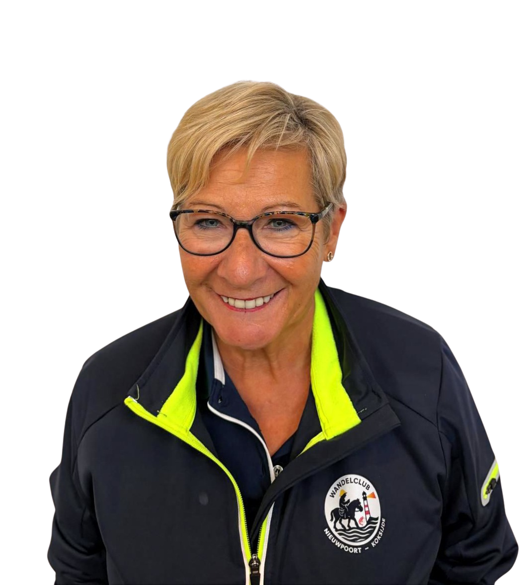 Een glimlachende vrouw met kort blond haar, bril en een donkerblauw jasje met geel accenten, met een logo van een wandelclub op de jas.