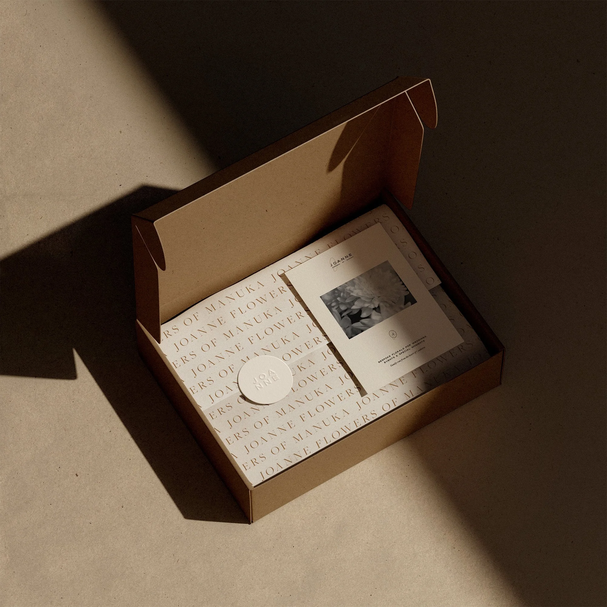 Open beige box with printed text and a card inside, sitting on a beige surface with shadows.