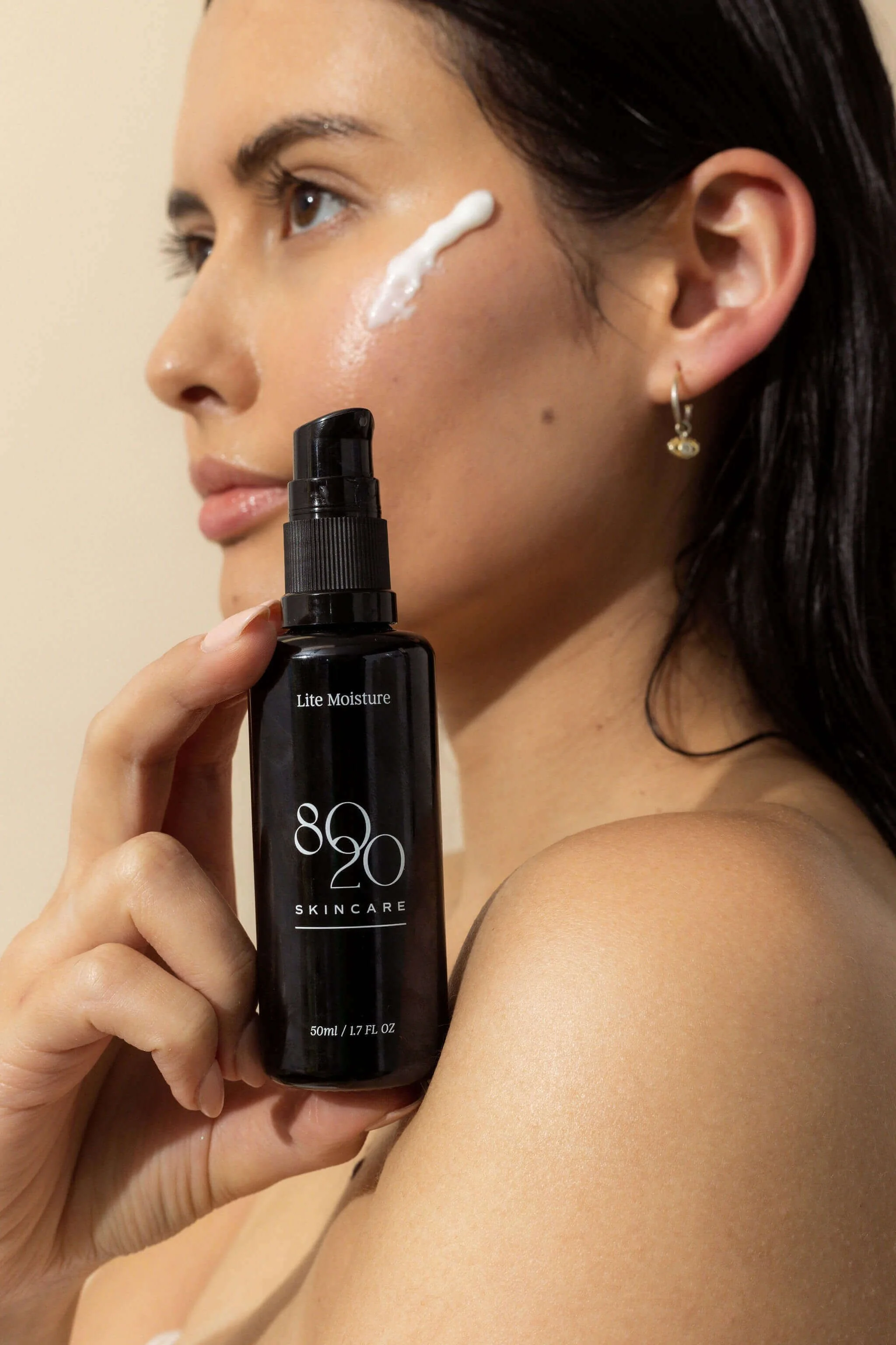 Woman applying moisturizer with 8020 Skincare bottle in hand.