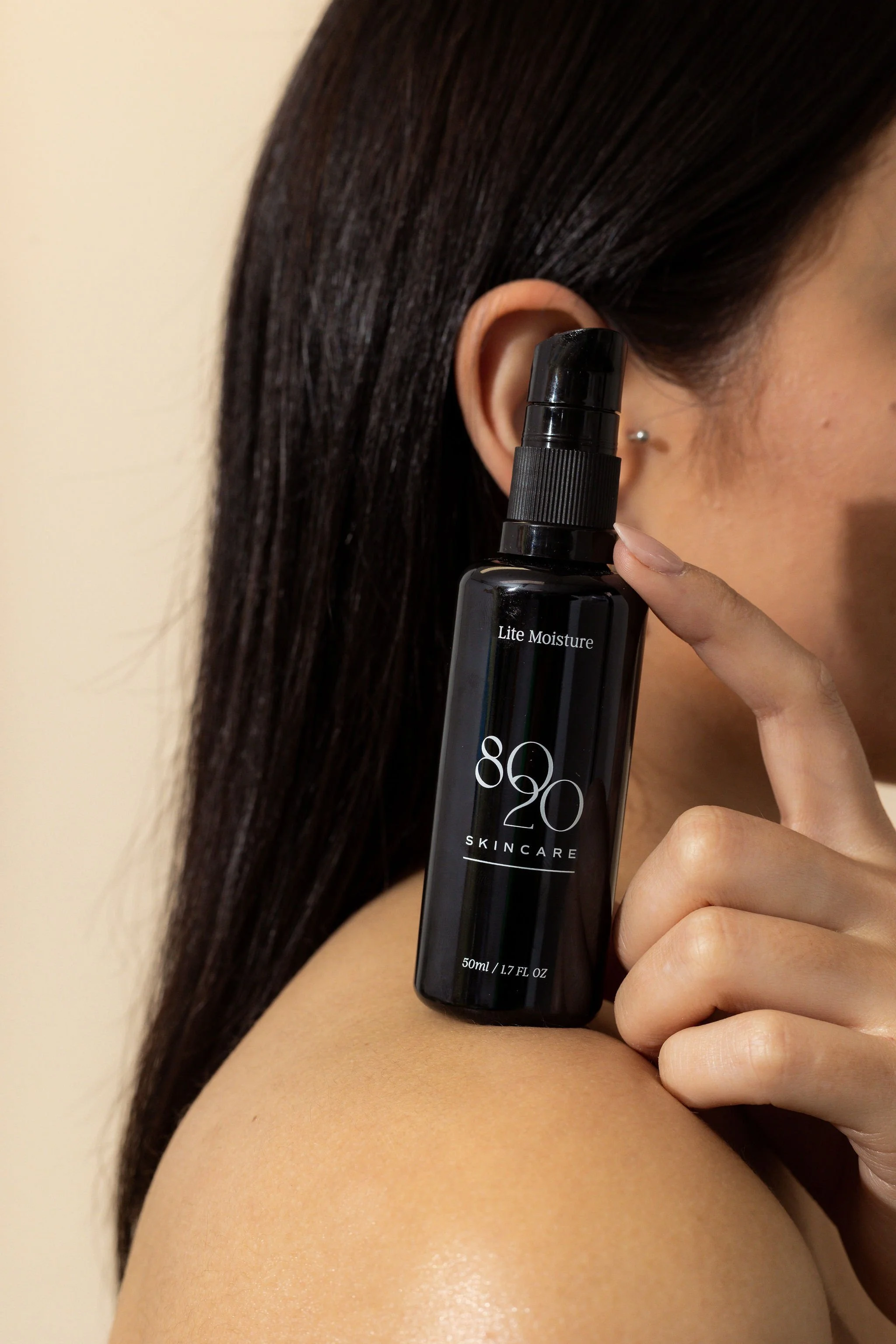Person holding a black bottle labeled "80 20 Skincare Lite Moisture" by their face.