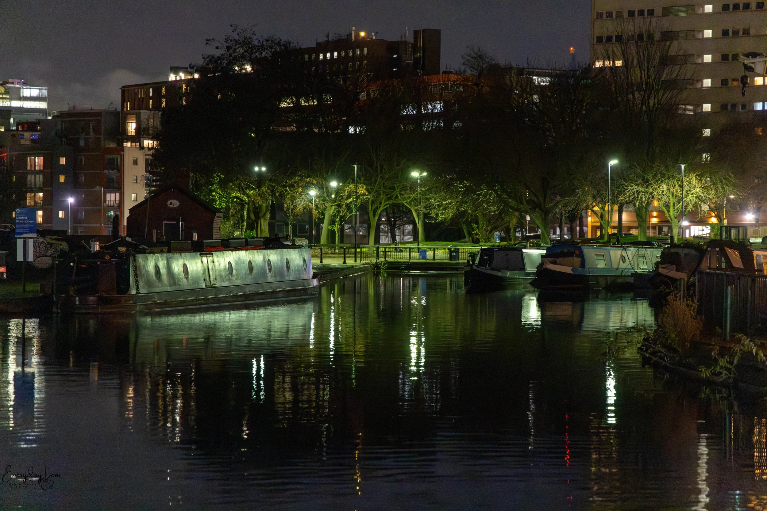 Moored boats beneath city lights, reflected on still water