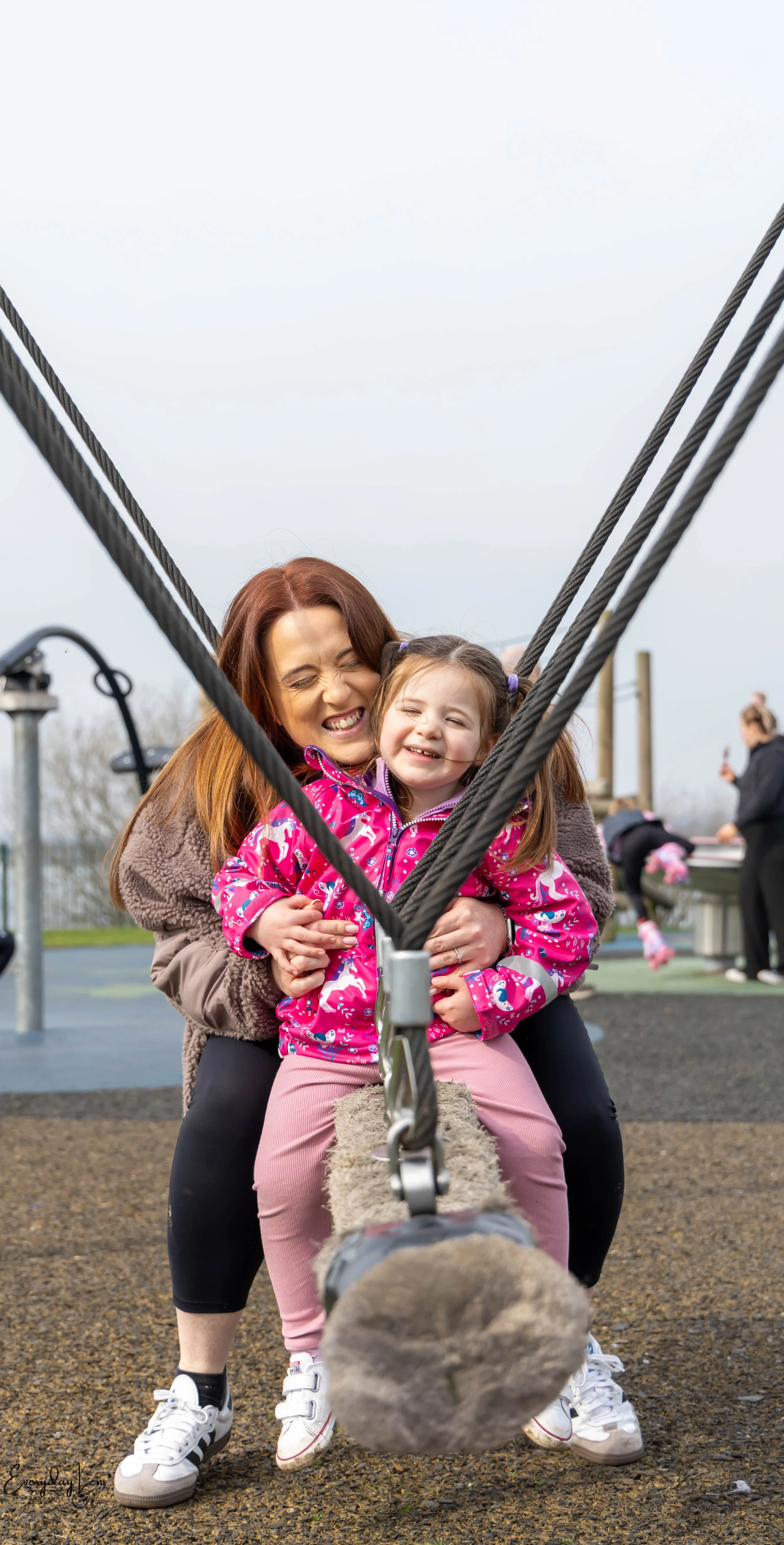 A woman and a young girl enjoying themselves on a playground swing, smiling and hugging each other.