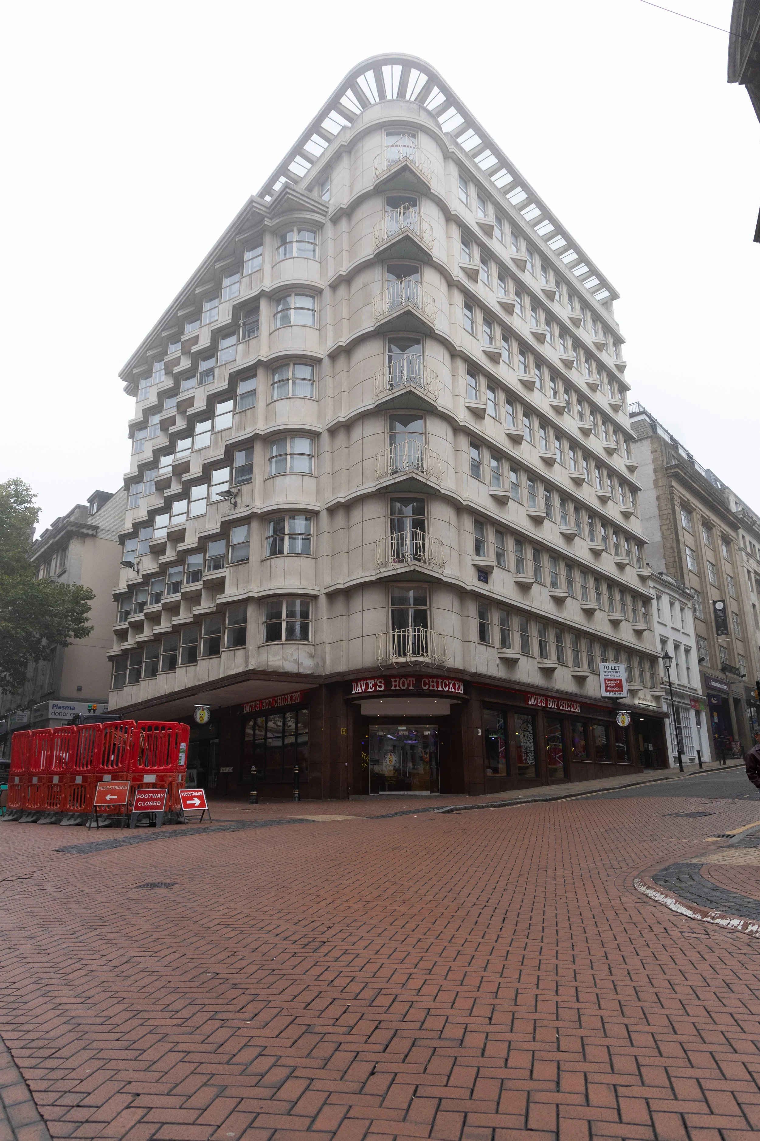 A multi-story white building with curved bay windows and small balconies on each floor, located on a city street with red brick paving. 
