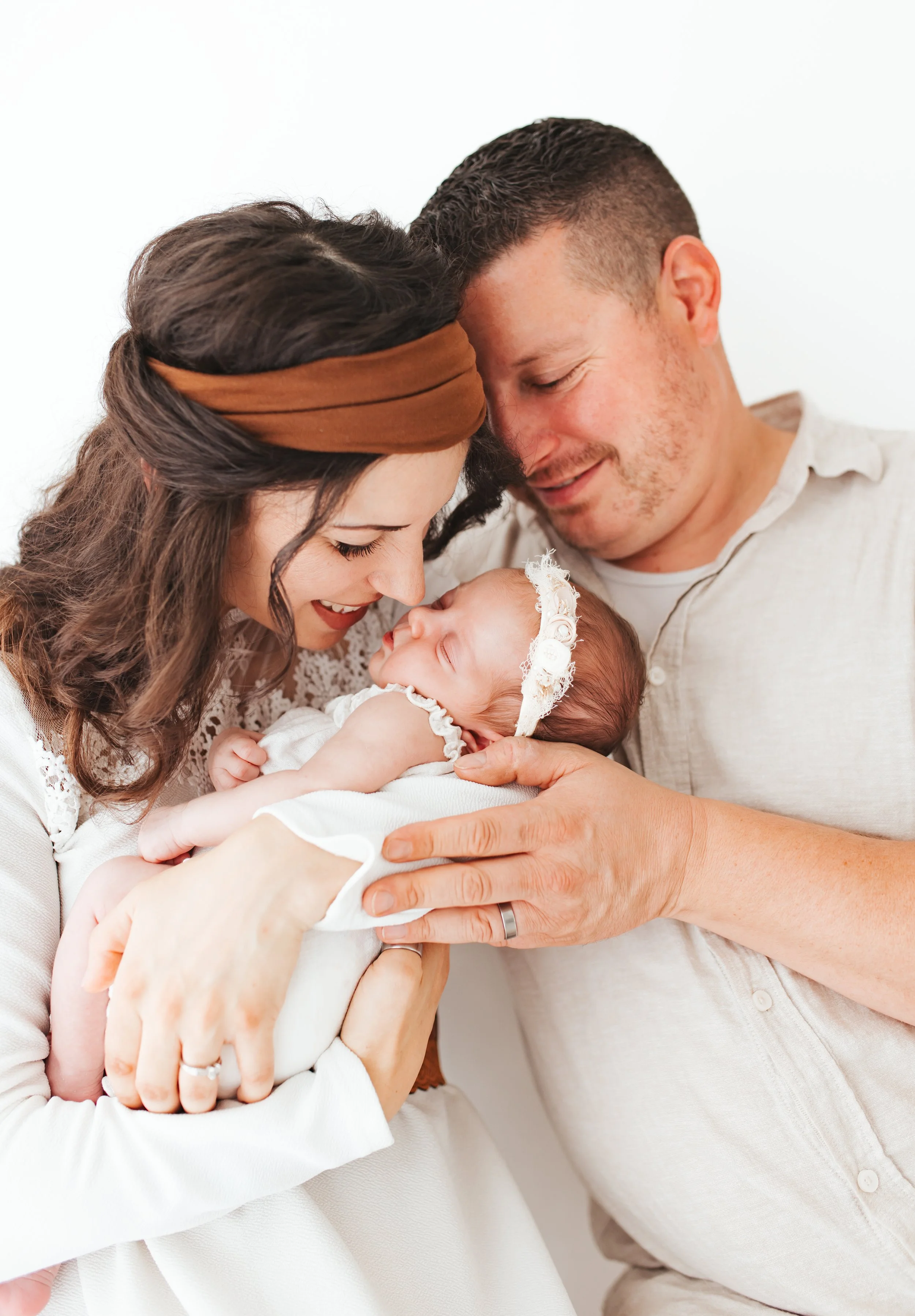 Ein glückliches Paar hält seine schlafende Baby-Tochter, die sie liebevoll ansehen, in einem hellen Raum.