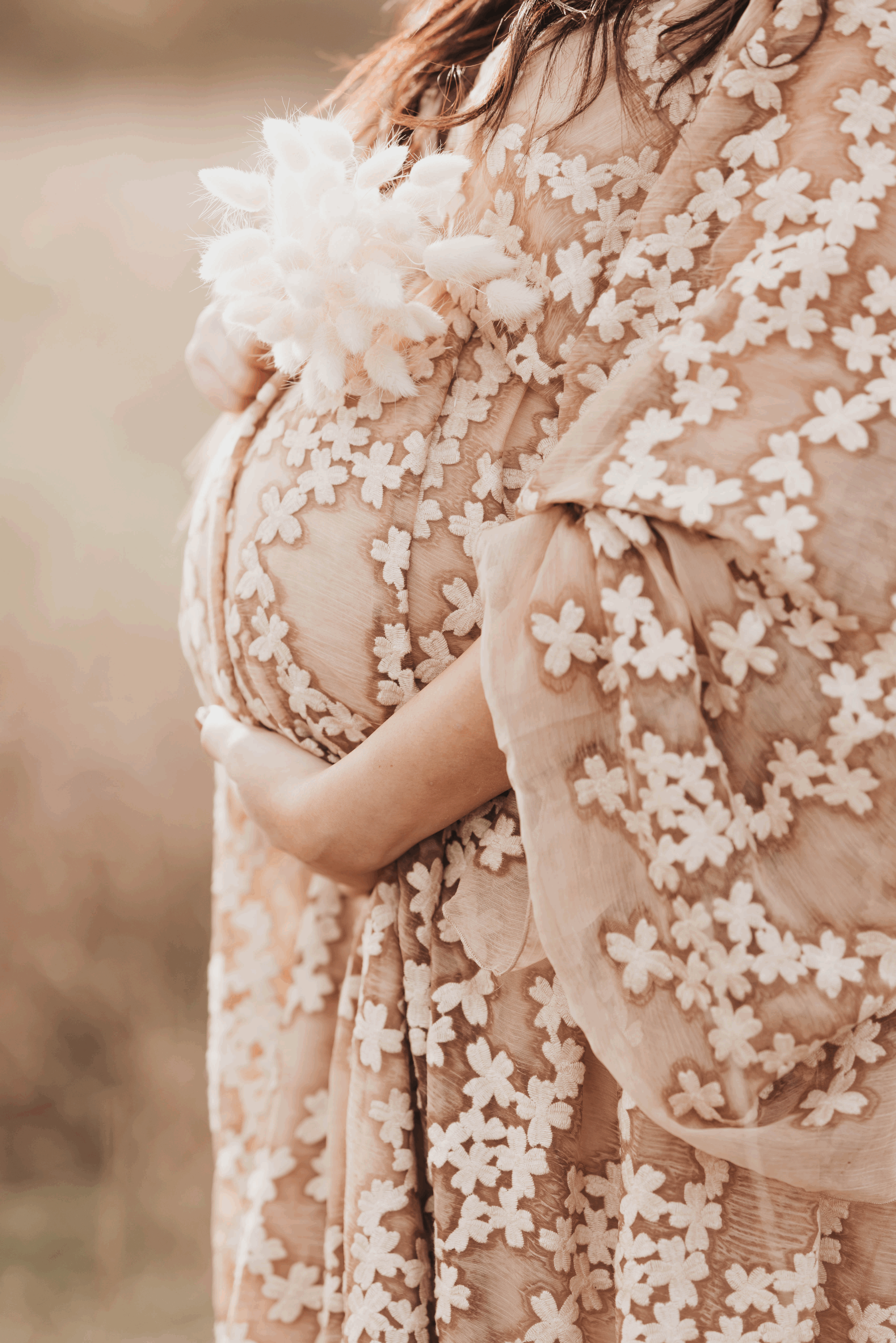 Nahaufnahme eines schwangeren Bauches in einem Kleid mit floralem Dekor, gehalten von einer Frau im Freien.