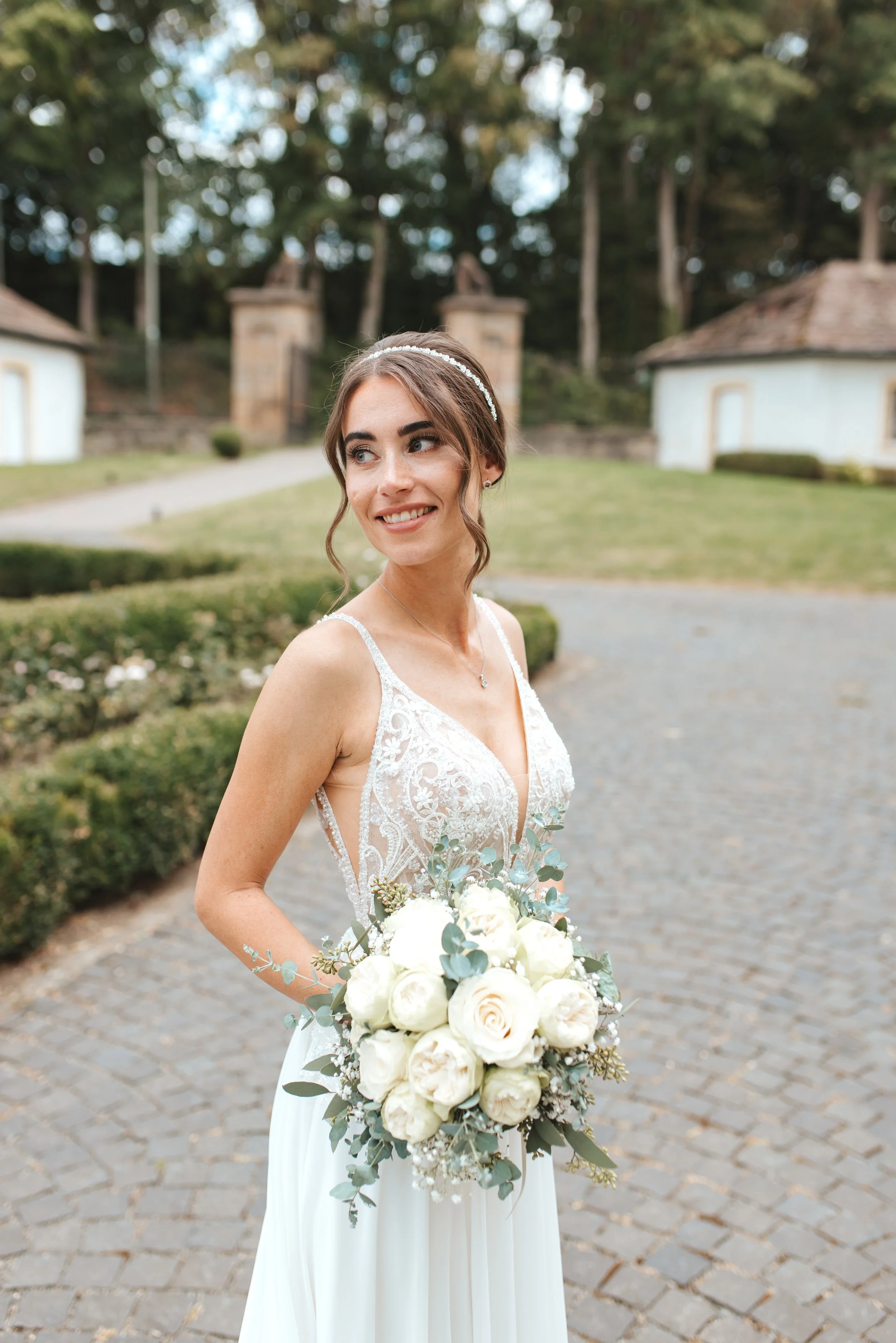 Braut in Brautkleid hält einen weißen Blumenstrauß bei einem Spaziergang im Park.