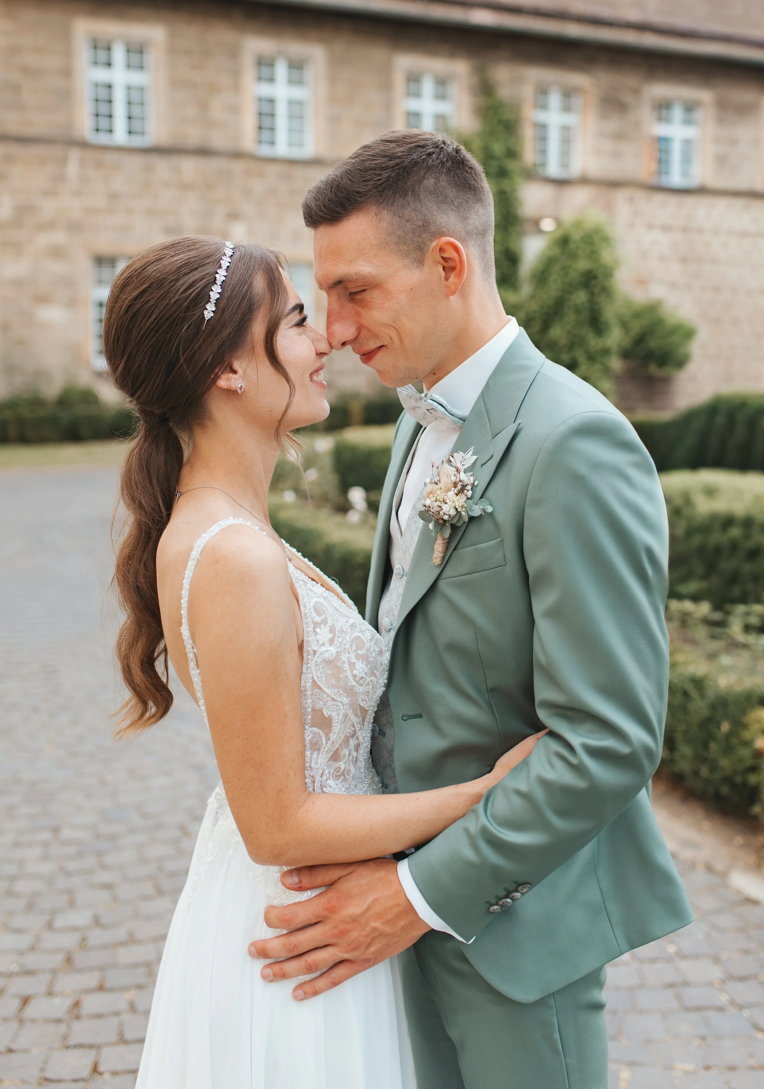 Ein Brautpaar steht sich bei einer Hochzeit draußen gegenüber, mit einem historischen Gebäude im Hintergrund.
