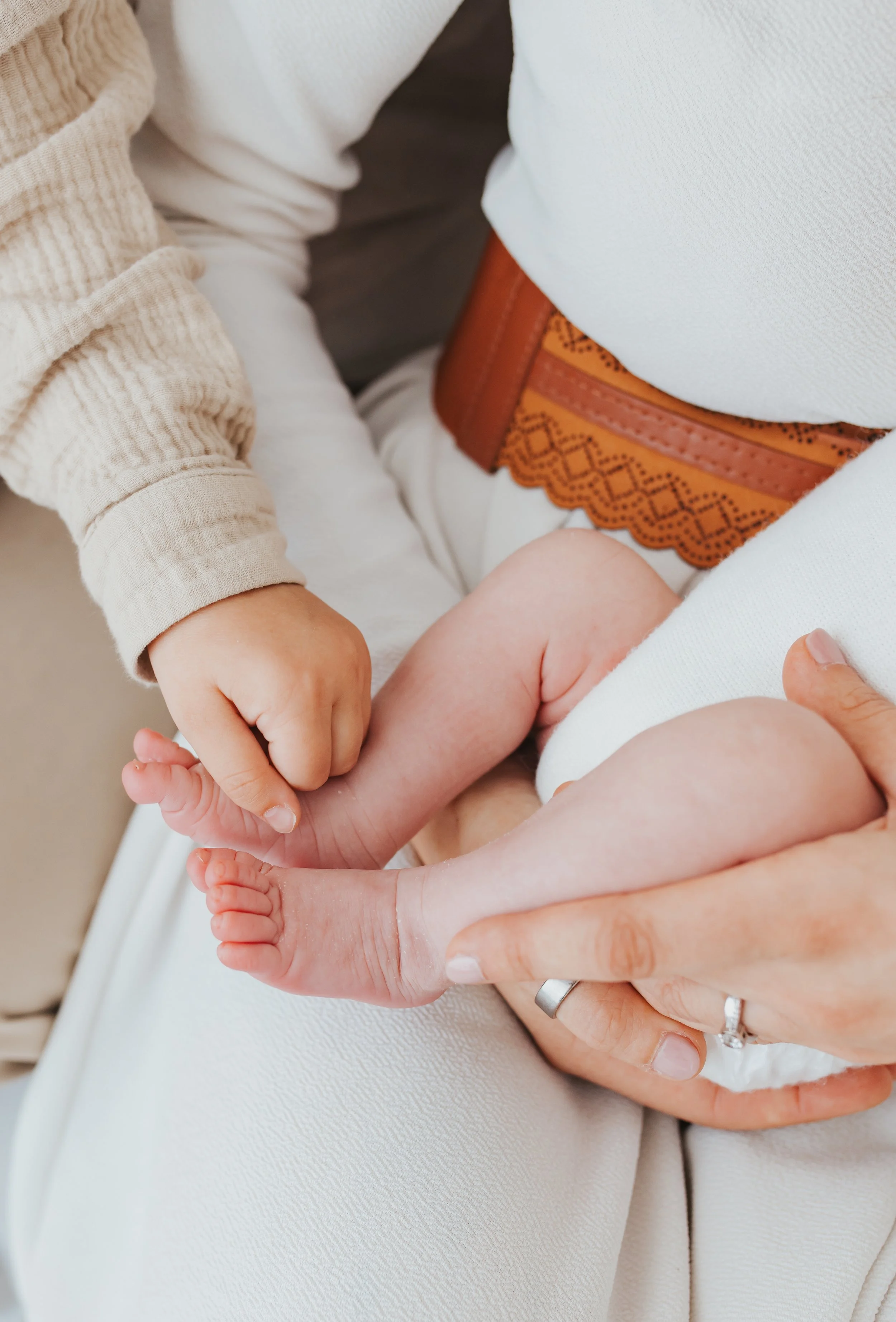 Ein Kind hält die Zehen eines Babys, das auf dem Schoß einer erwachsenen Person liegt.