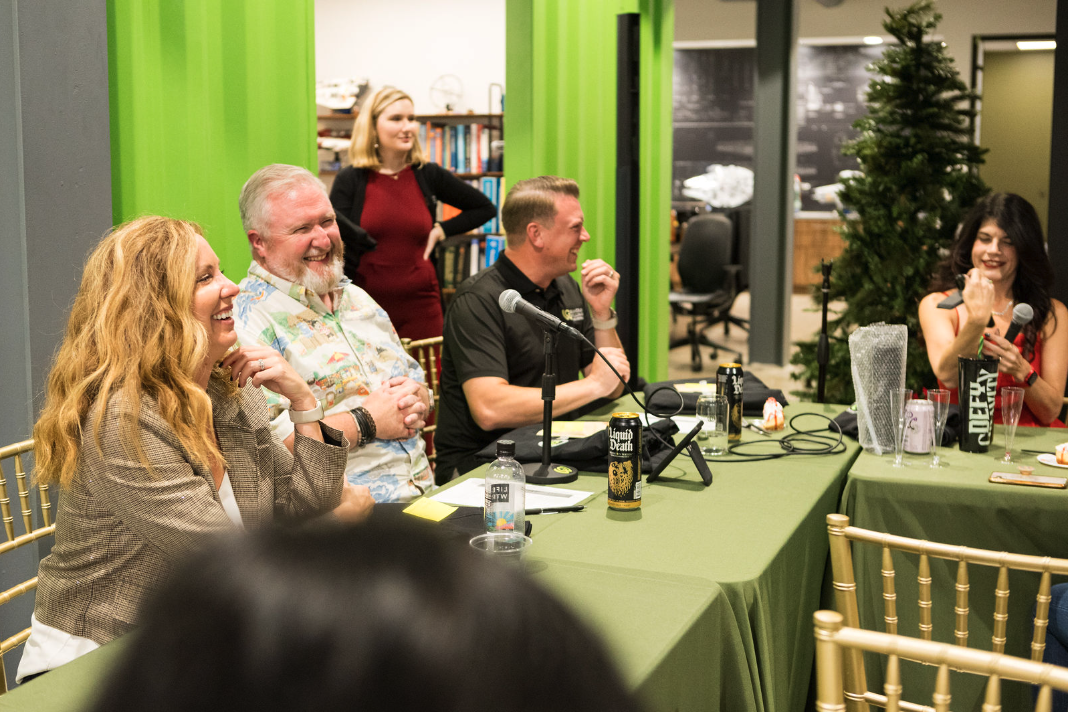 People sitting at a table, laughing, and smiling during a discussion or podcast in a decorated indoor space.
