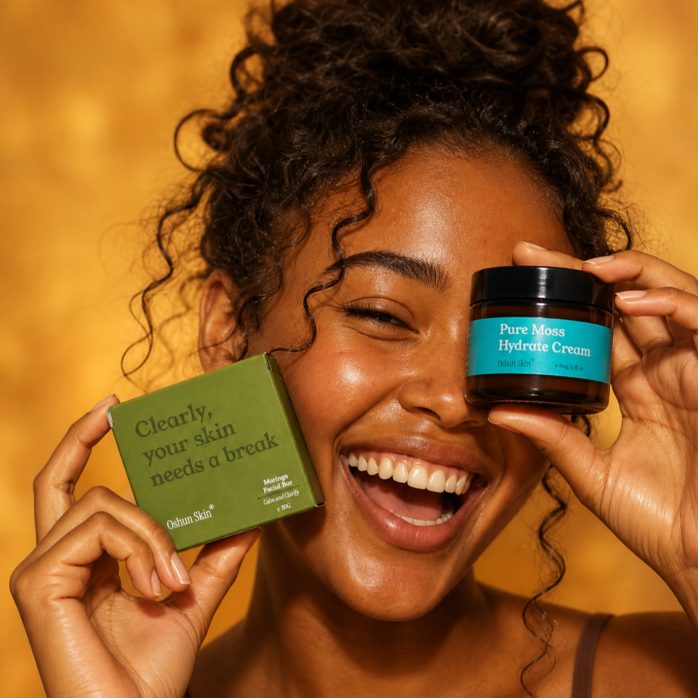 A+young+woman+with+rich-toned+glowing+skin+laughing+openly%2C+holding+Moringa+Soap+Box+up+to+one+cheek+and+the+Pure+Moss+Hydrate+Cream+over+eye.png