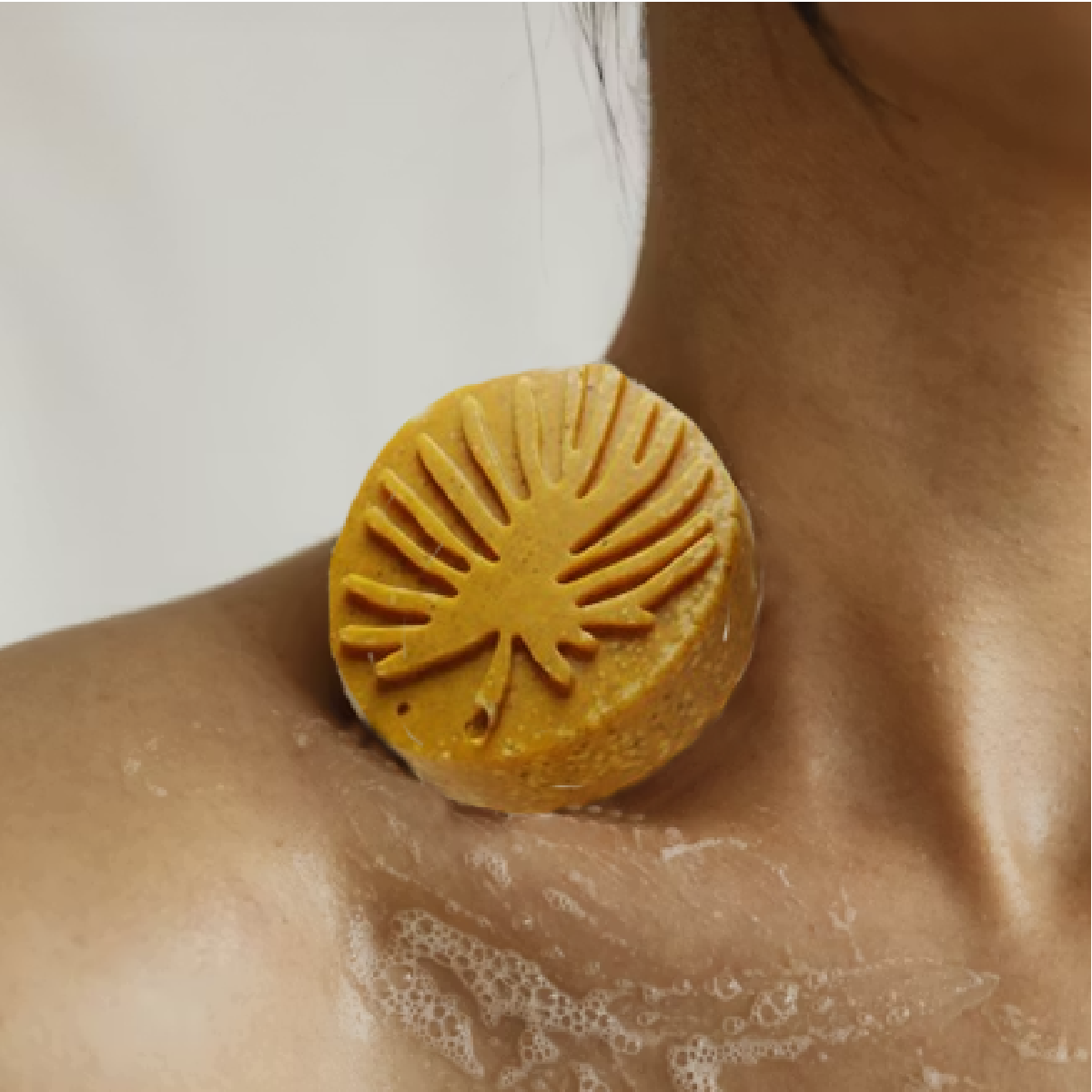 A single turmeric leaf botanical design bar placed on a woman's collarbone with lathered bubbles
