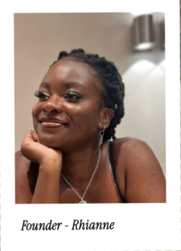 Portrait of a woman with braided hair, smiling with her hand resting on her chin, wearing earrings and a necklace, in an indoor setting.