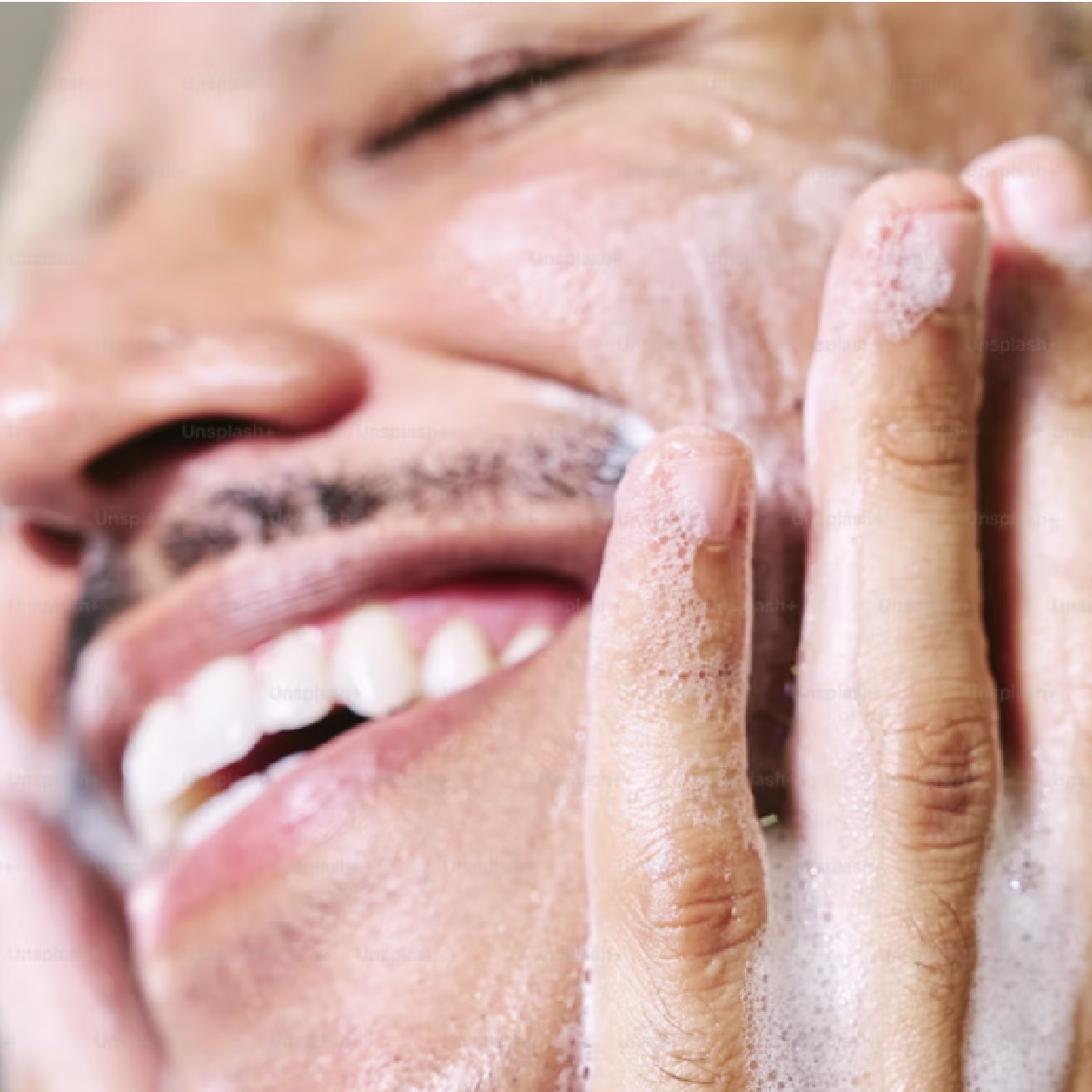 An upclose shot of a man smiling while lathering soap on face