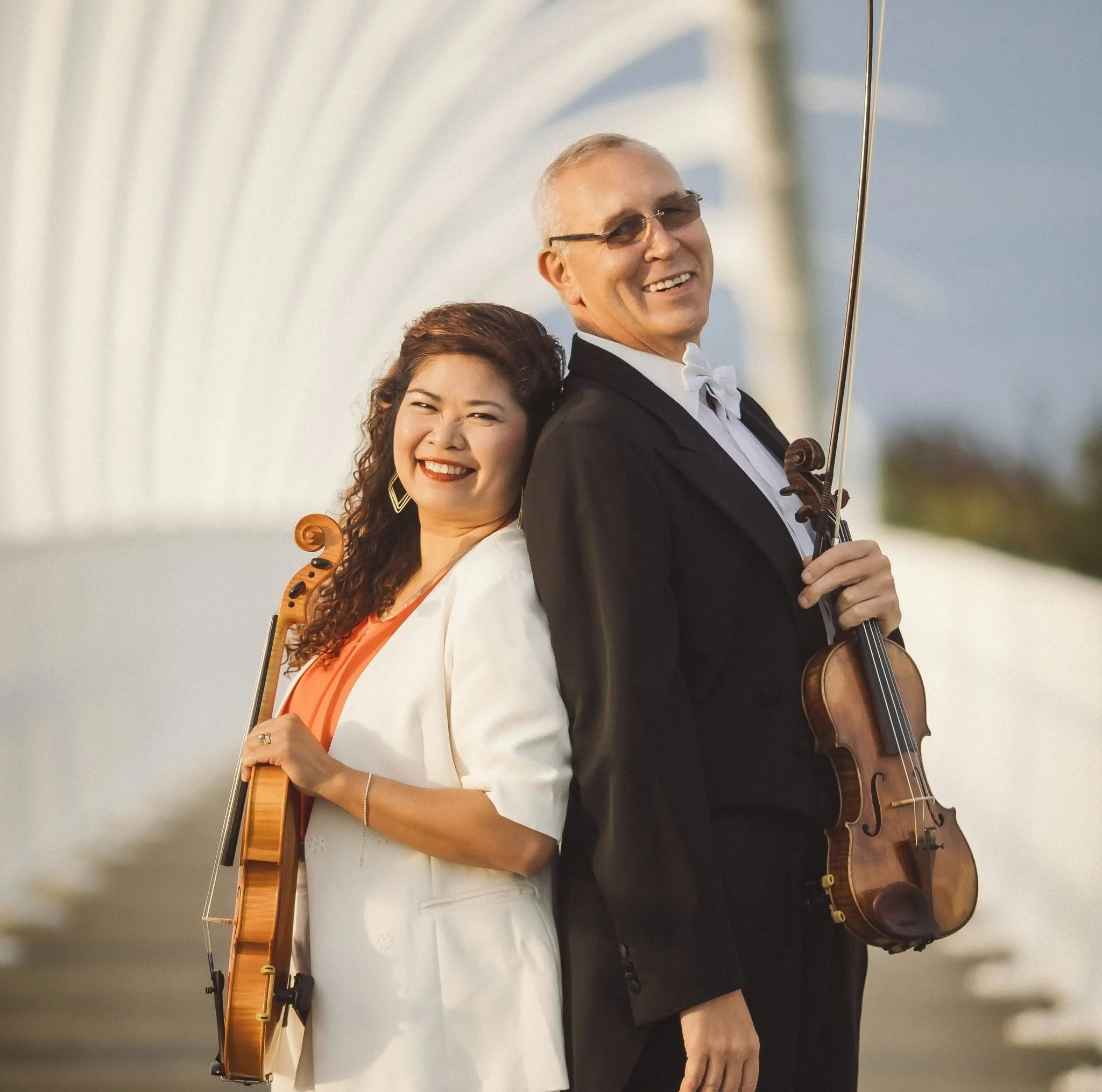 Two Crescendo musicians, Lyly King and Albert Klin, dressed in formal attire, are holding violins and standing back to back on the iconic Te Rewa Rewa bridge in Taranaki.