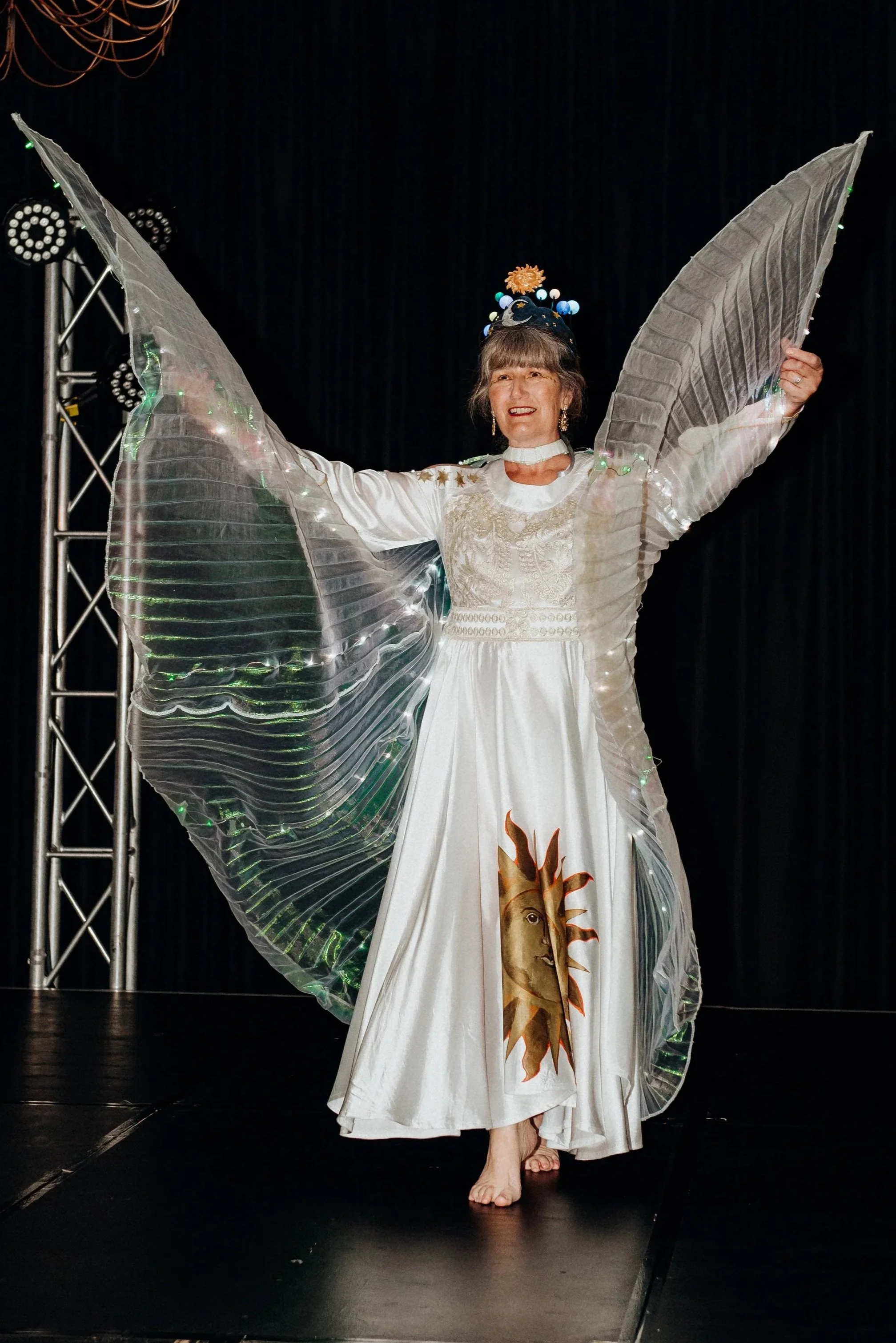 Bronwyn Hughes presents a celestial dance inspired by her heritage, in a handmade costume and headpiece with small planets and a sun, swirling a pair of LED Isis wings.